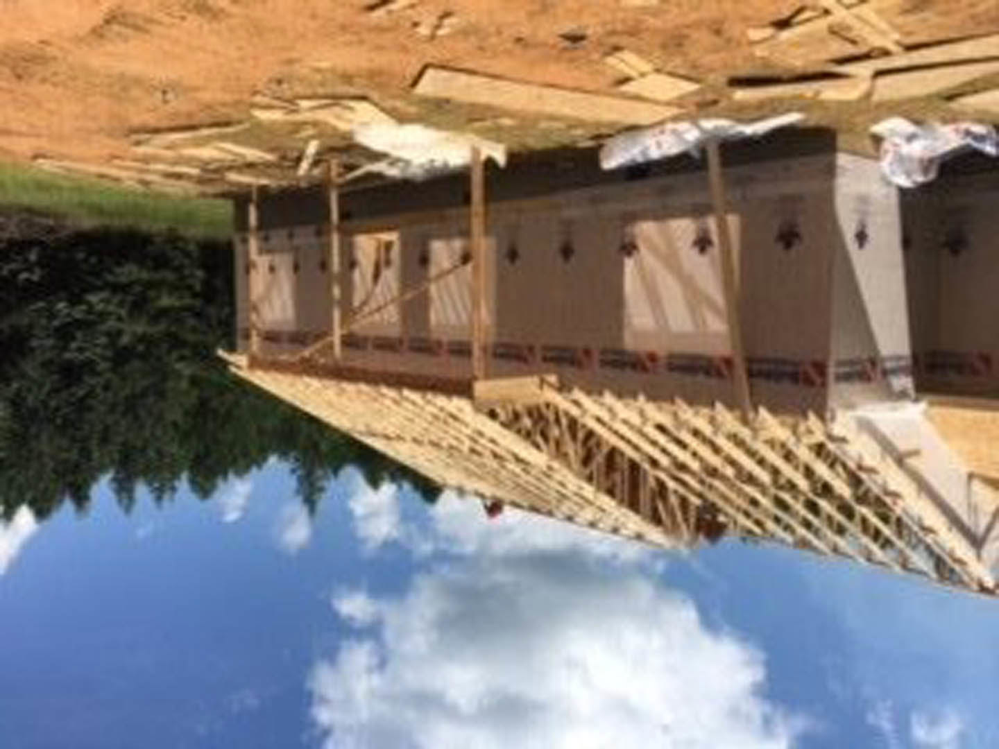 Wood-framed custom home under construction with exposed beams, unfinished exterior walls, and cloudy sky in background