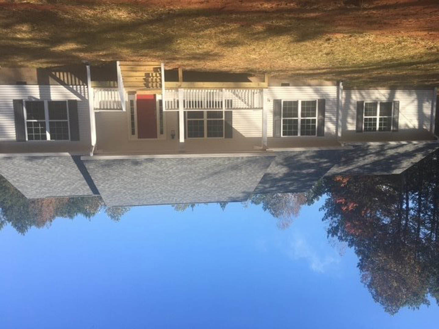 Red front door and white-framed windows on a house with a covered porch, surrounded by green lawn
