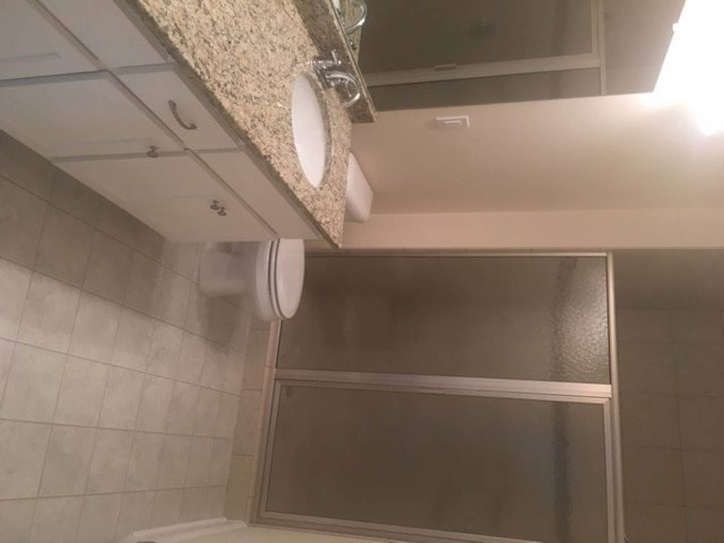 Bathroom featuring a marble countertop with an undermount sink, white tile flooring, plaster walls, and a partial view of a toilet and walk-in shower.