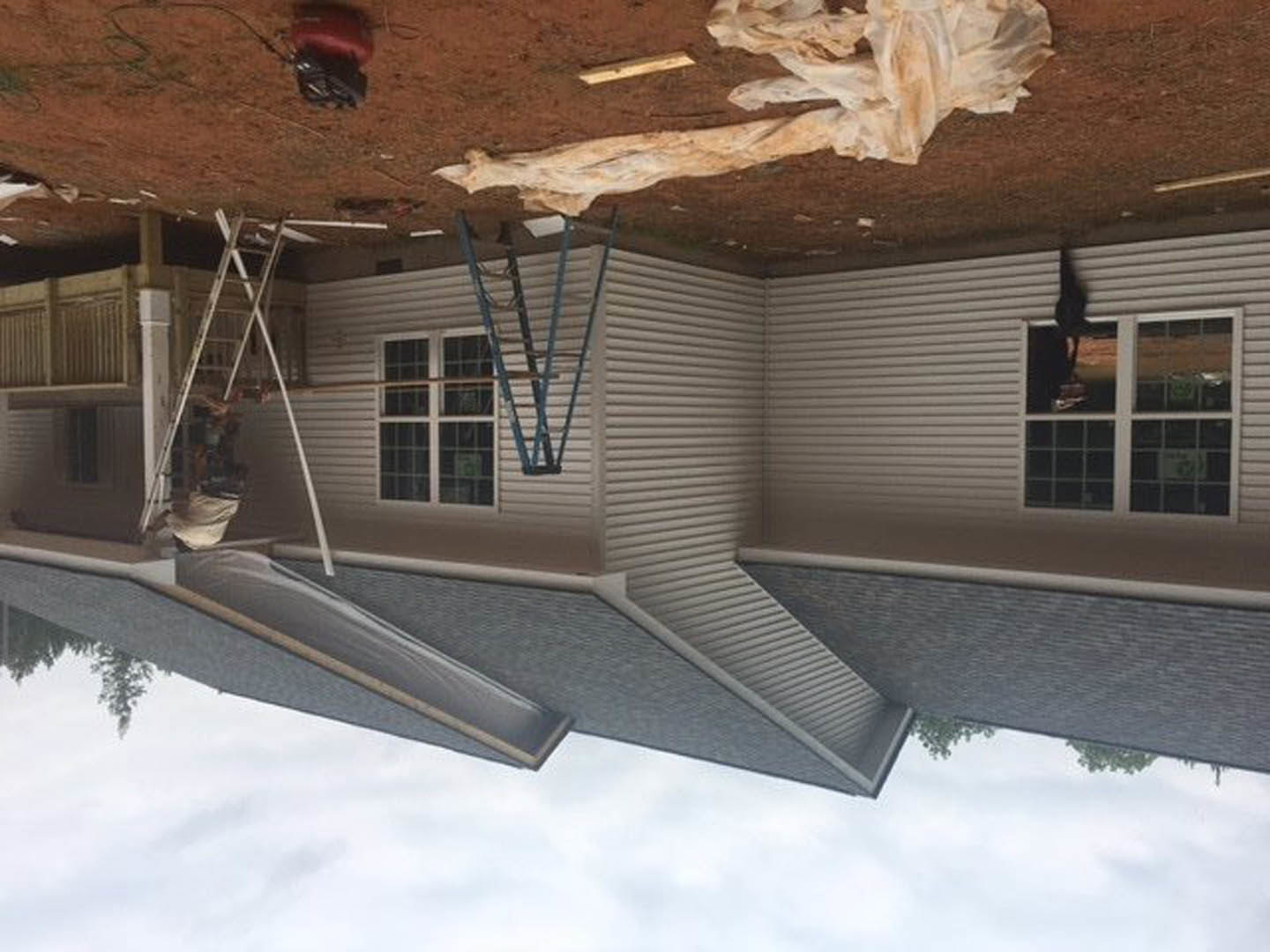 Scaffolding surrounds a partially finished house with exposed siding, construction materials piled nearby, and a ladder leaning against the exterior; snow covers the ground and a