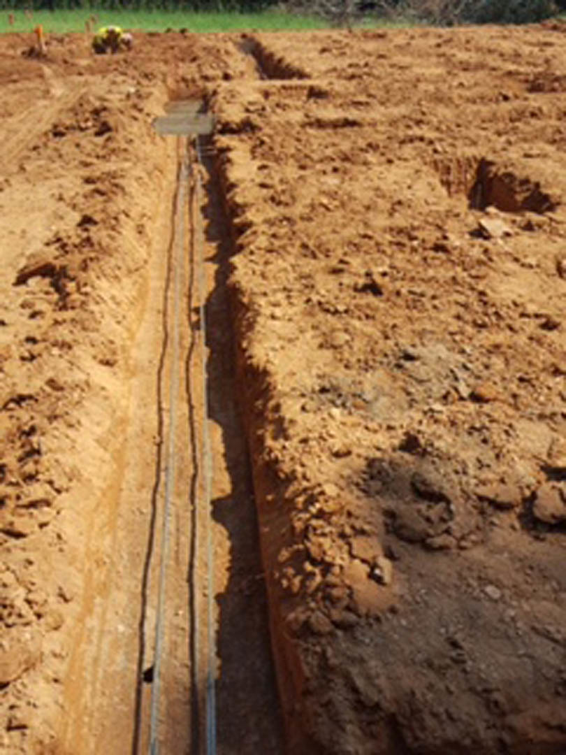 Narrow dirt trench with exposed soil and tire tracks, outdoor construction site