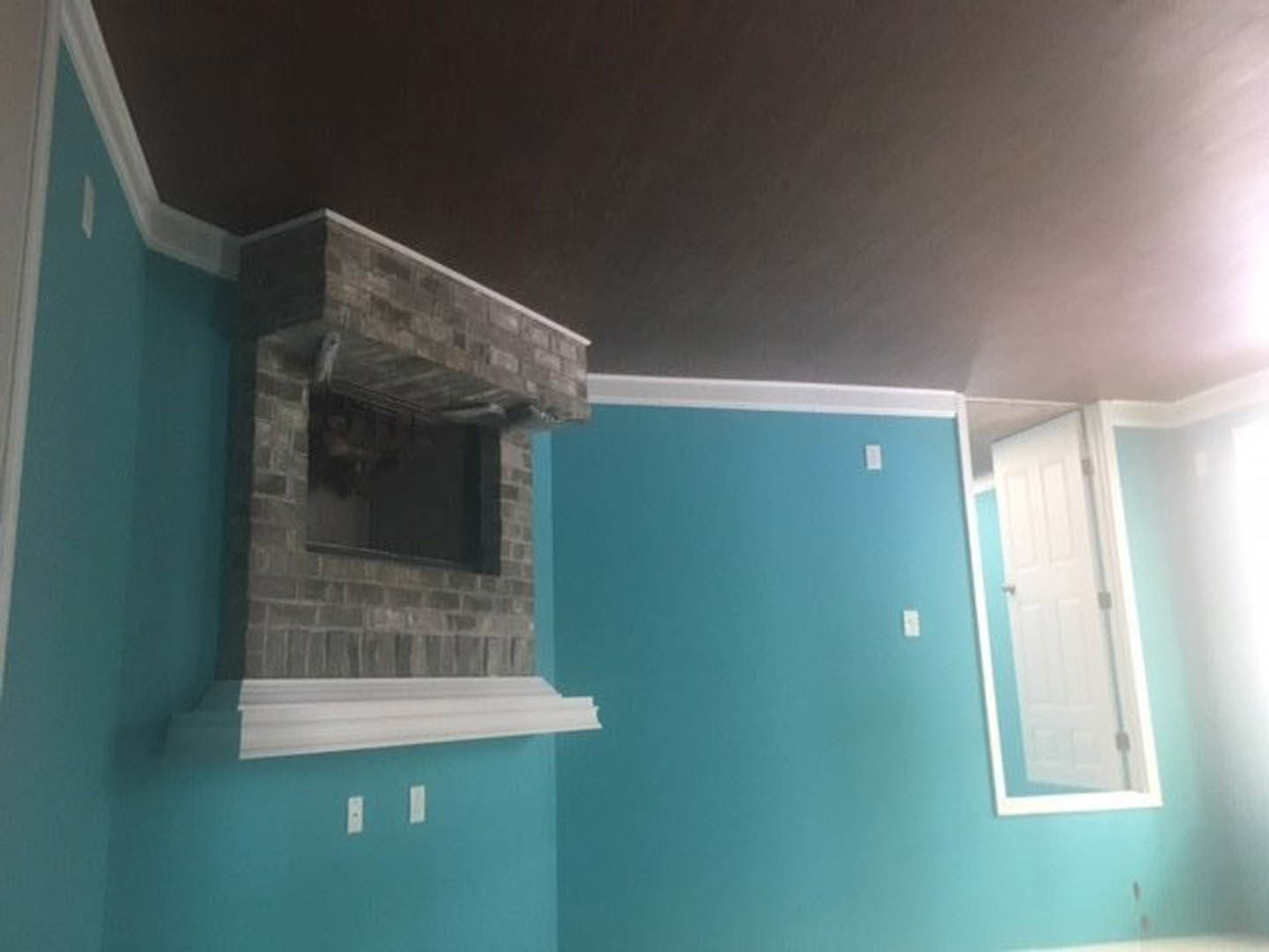 Brick fireplace with white mantel in blue-walled living room, white door and window with trim, plaster ceiling, hardwood floor