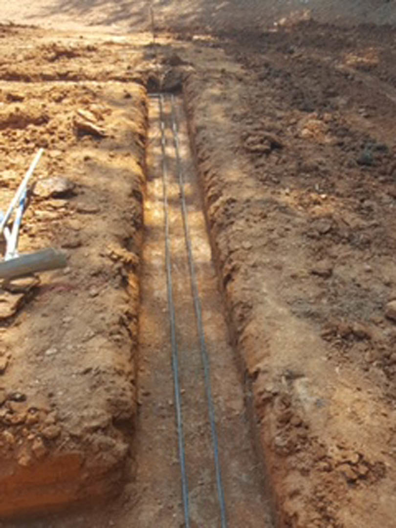 Open trench in soil with exposed electrical wires running along the ground outdoors