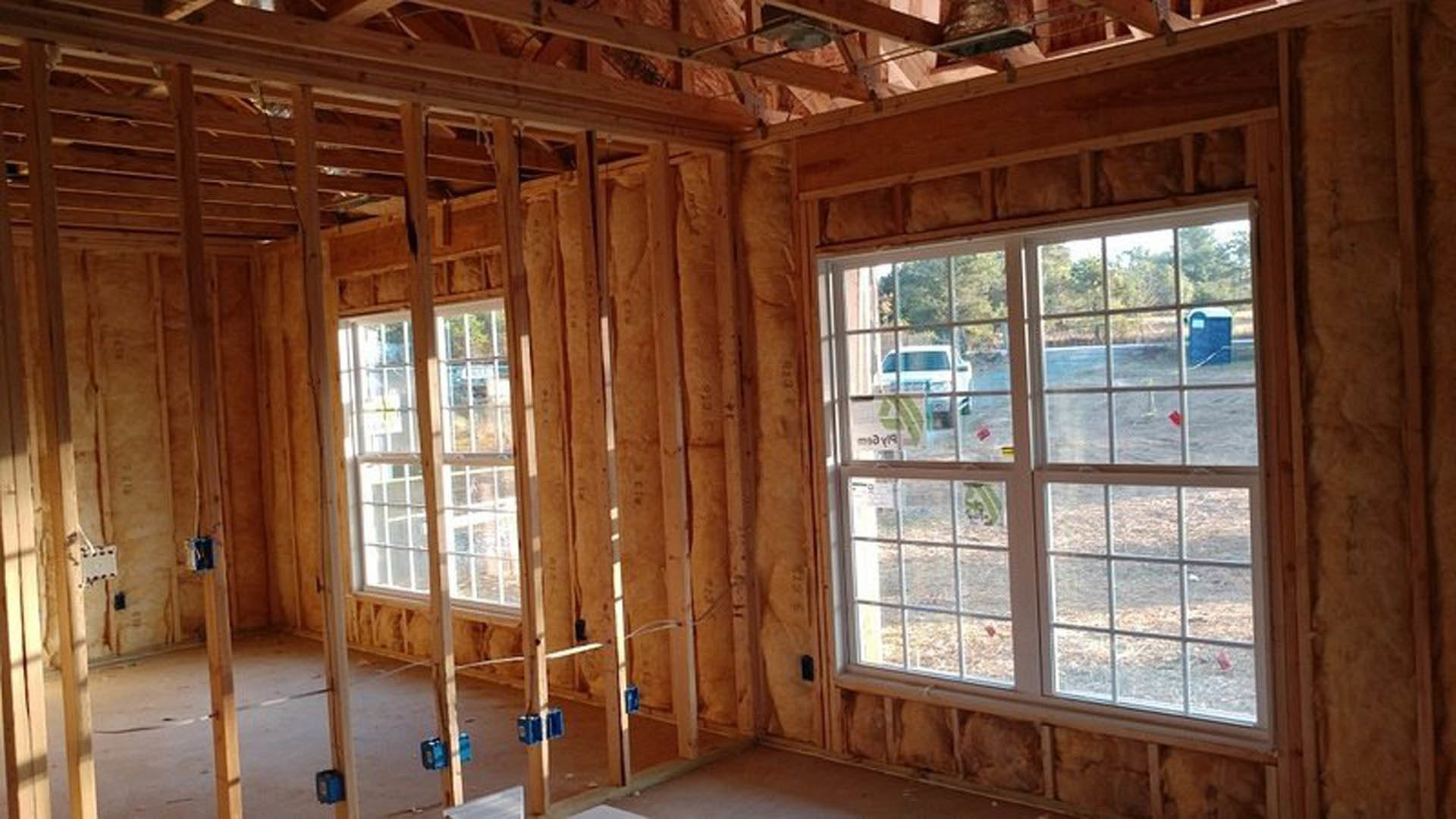 Living room with exposed wood ceiling beams, large windows, and hardwood flooring