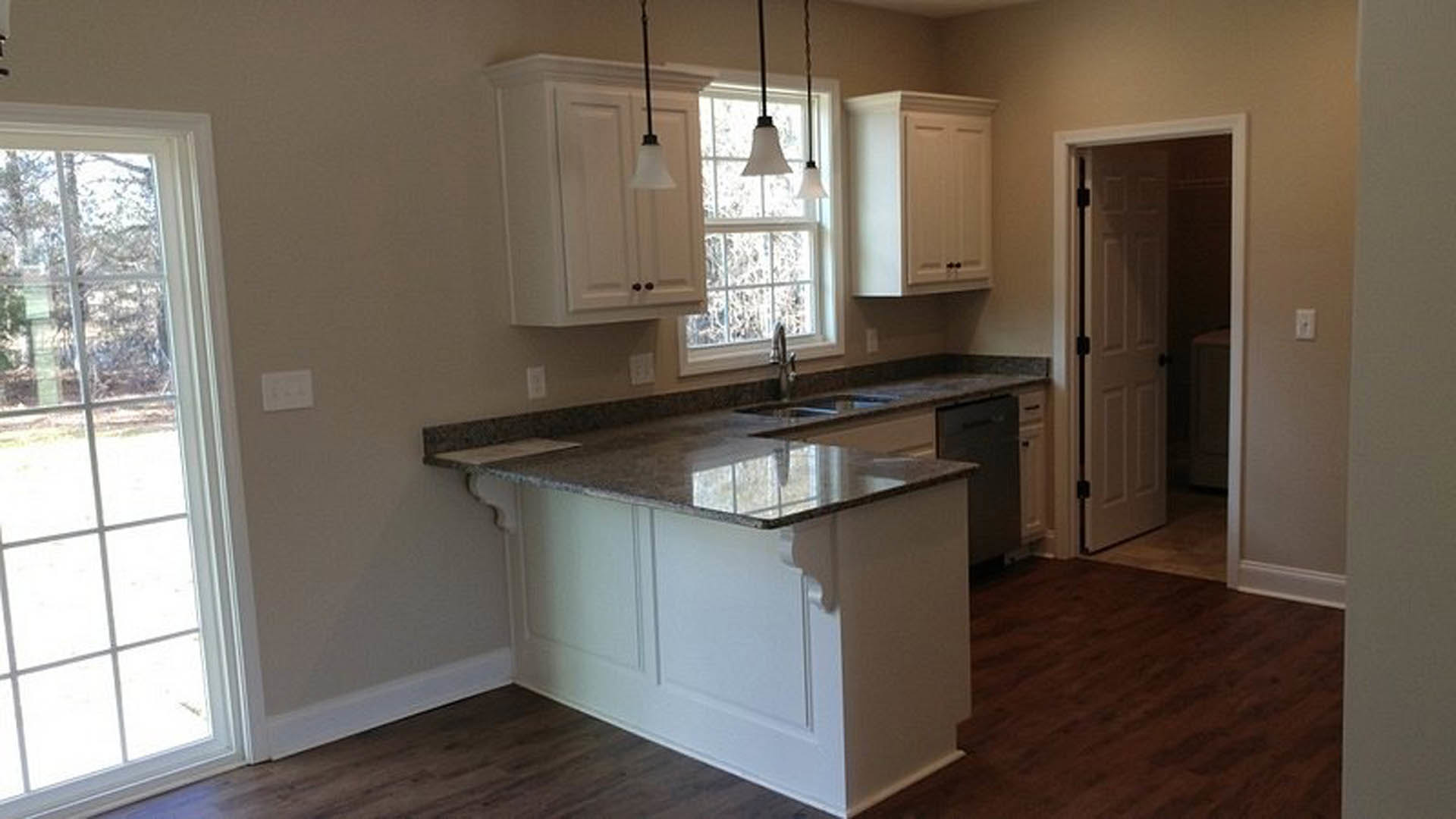 Granite countertop kitchen with white cabinetry, stainless steel sink, white door with black knobs, window overlooking outdoors, pendant light fixture, and white kitchen island