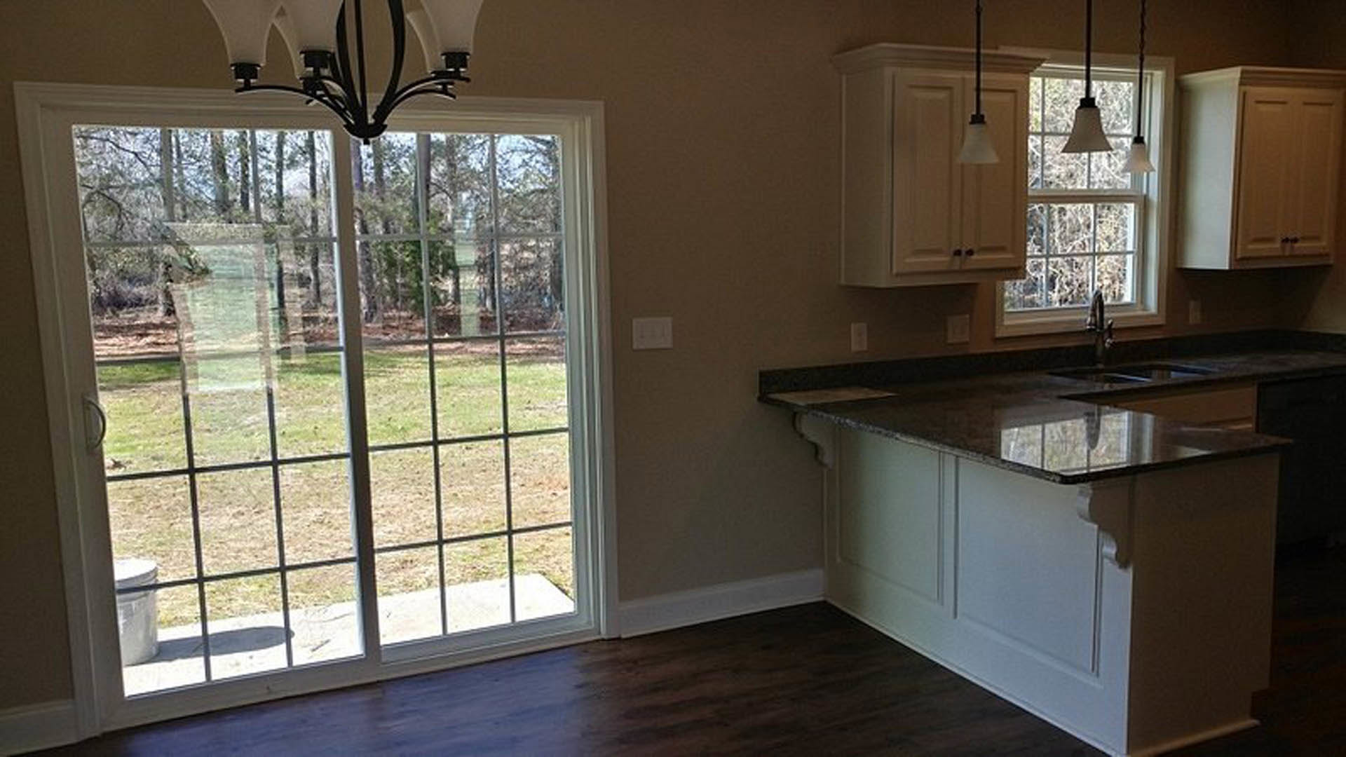 Modern kitchen featuring a glass door opening to a yard, white cabinetry with black hardware, central island with built-in sink, light wood flooring, and a contemporary chandelier