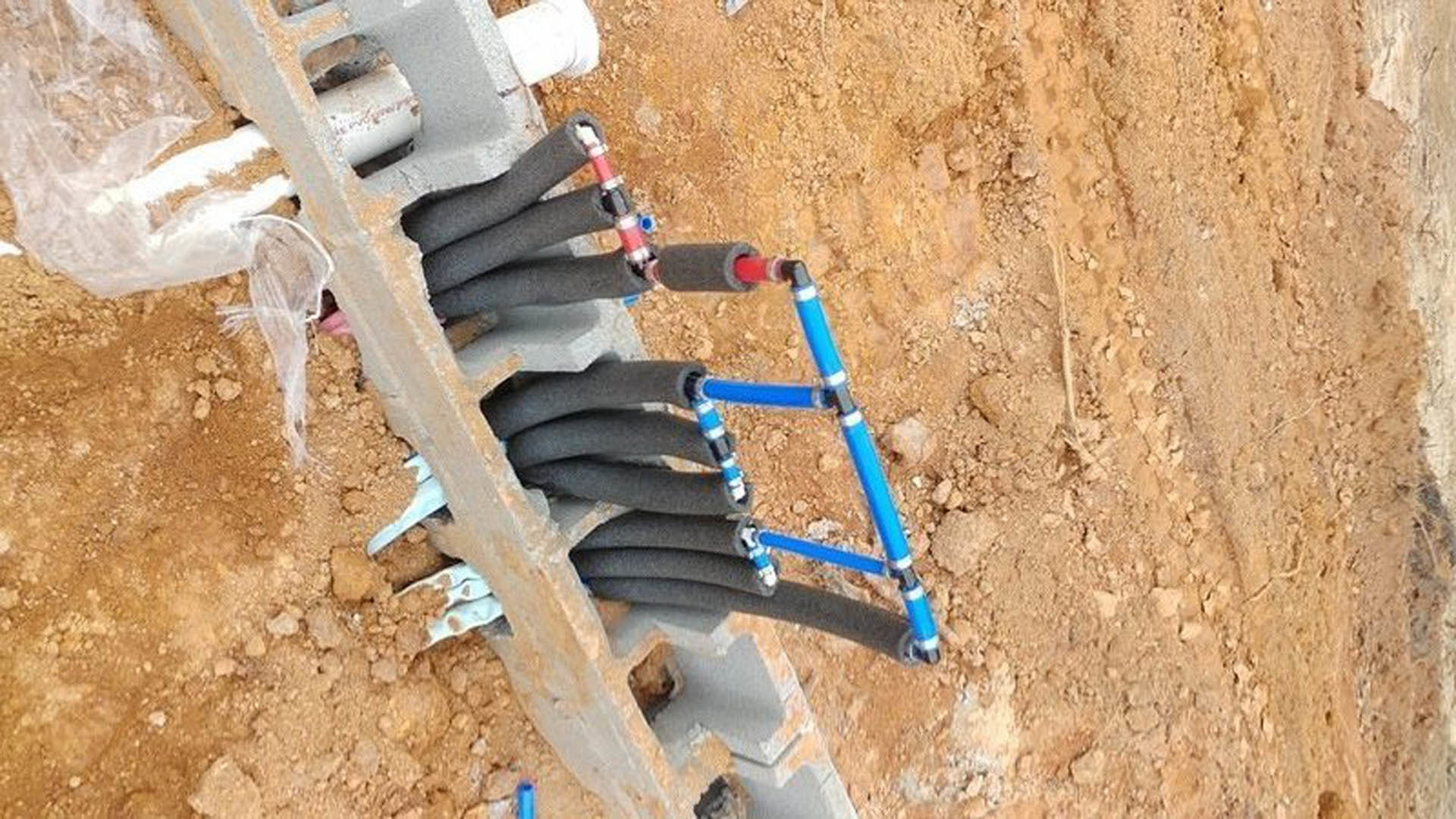 Grey and black pipes embedded in soil and concrete block, connected to an exterior wall