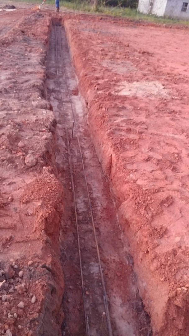 Freshly dug trench in brown soil outside, bordered by grassy ground and dirt tracks