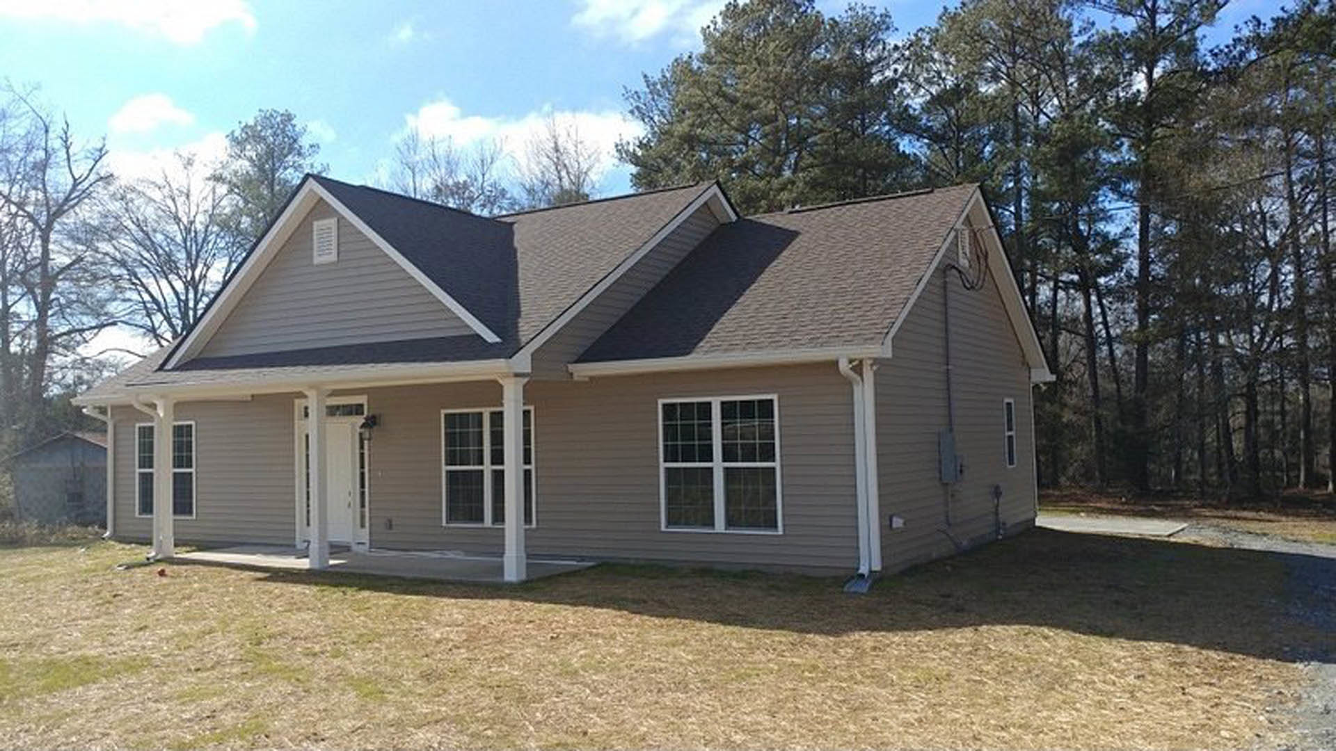 Two-story house with light siding, white-framed windows, white front door, covered porch, and green grass lawn; mature trees in background.
