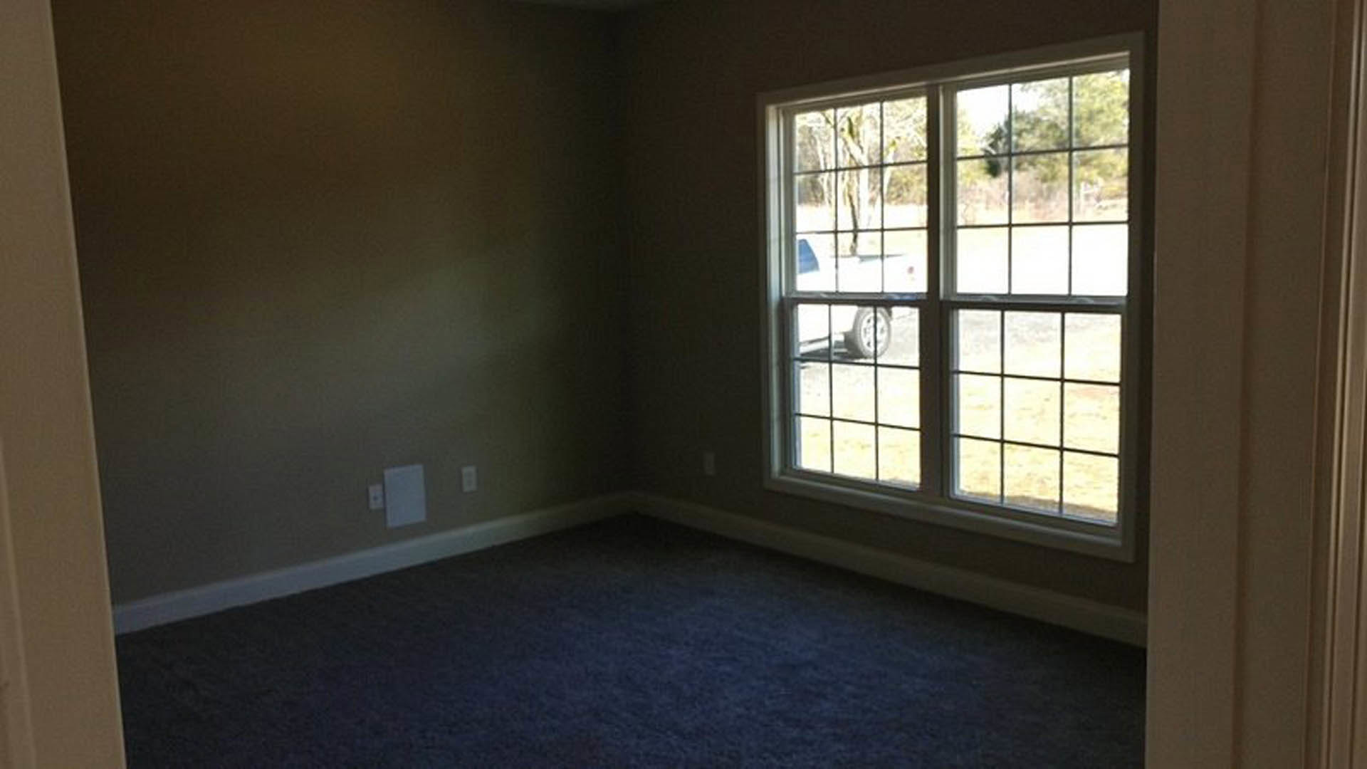 Blue carpeted floor in a room with white walls and a large window, car visible outside through glass