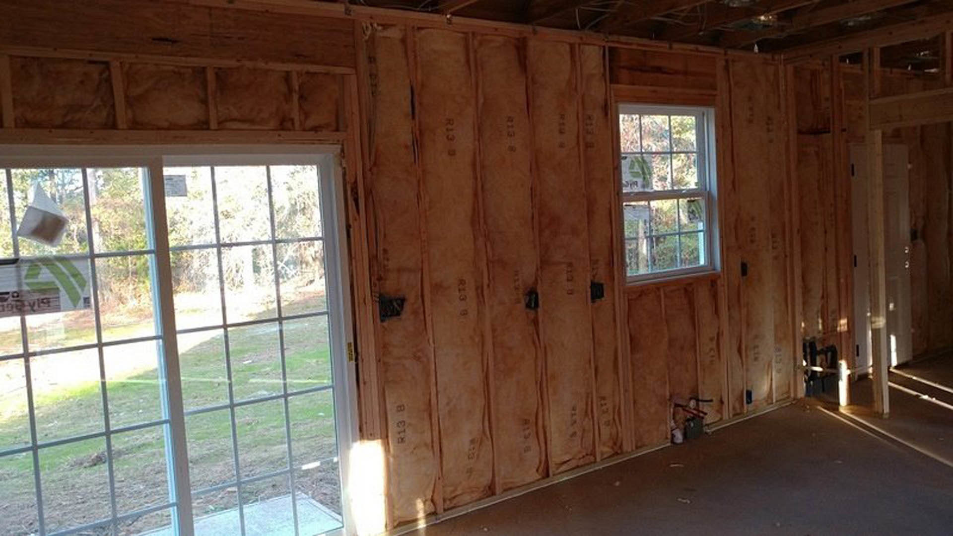 Spacious room featuring large multi-pane windows, wood-paneled walls, light hardwood flooring, and a built-in wooden cabinet