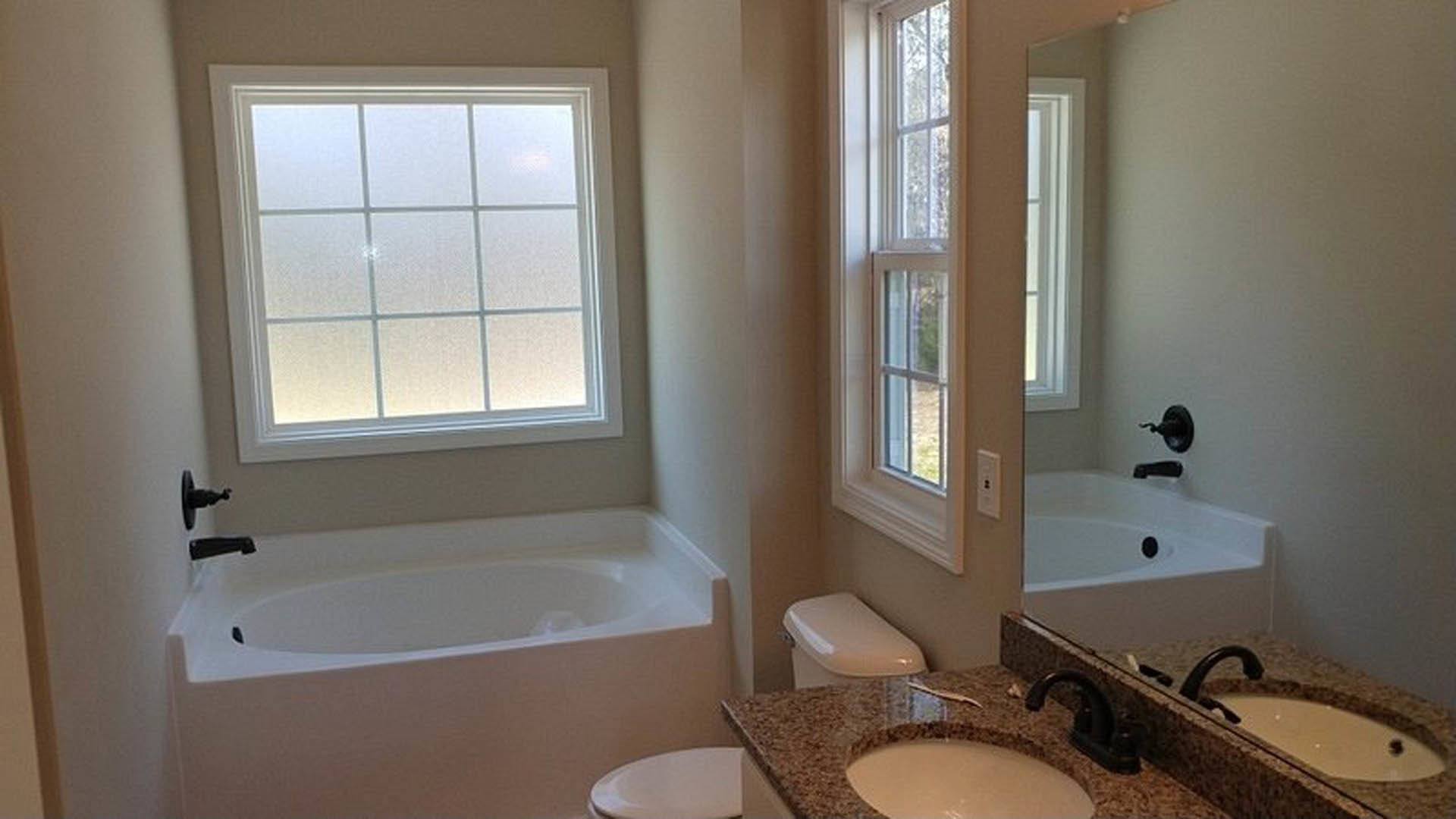 Modern bathroom with freestanding white bathtub, rectangular sink on wood vanity, large wall mirror, light gray tile walls, chrome faucet, and frosted window for natural light