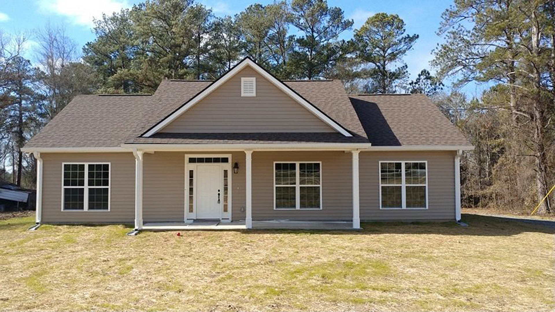 Brick house with white siding, glass-paneled white door, front lawn, mature trees, and small white house visible in the background