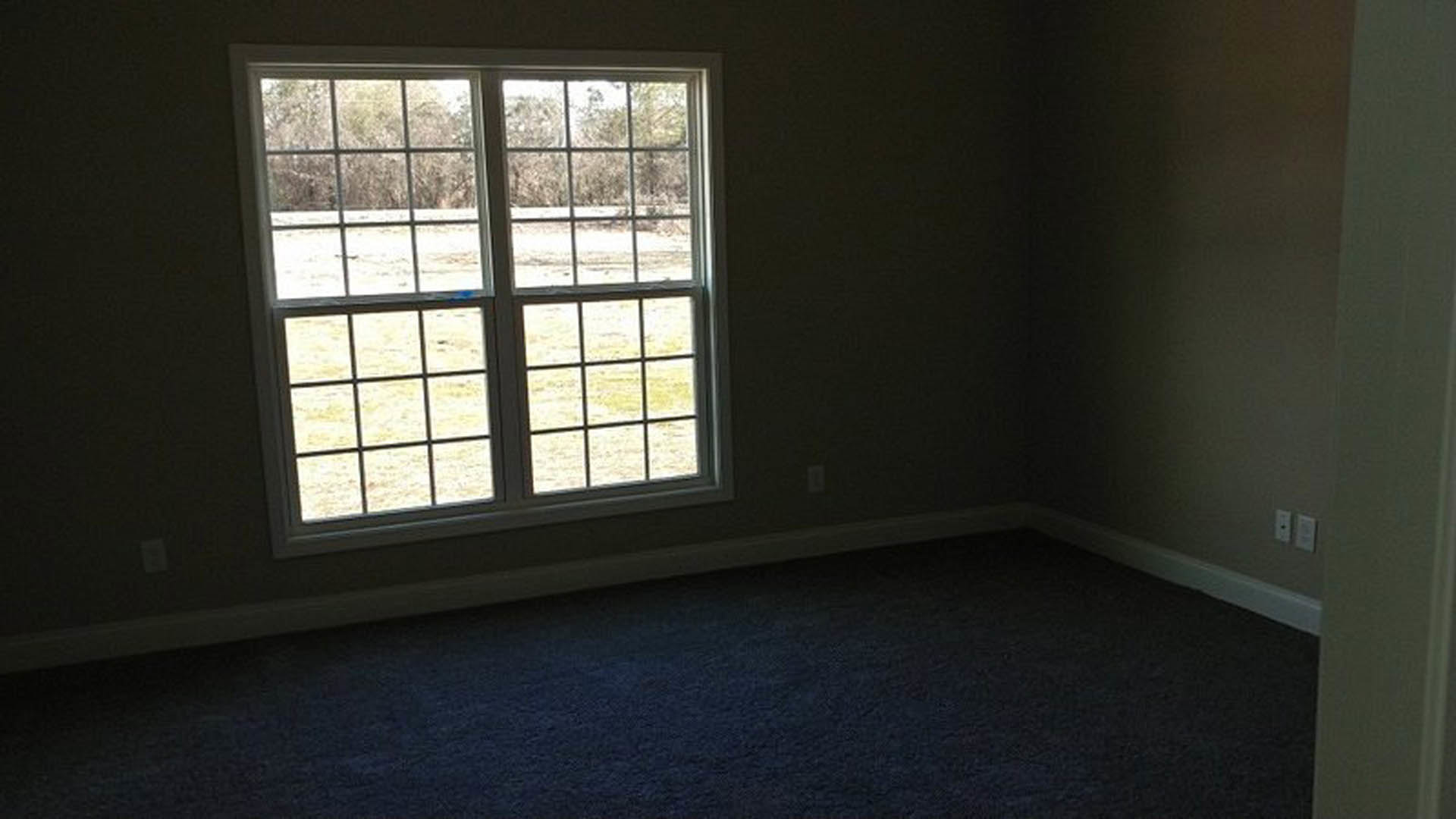 Bright room with large window overlooking grassy field, light wood flooring, white walls, and black countertop with white rectangular decor object