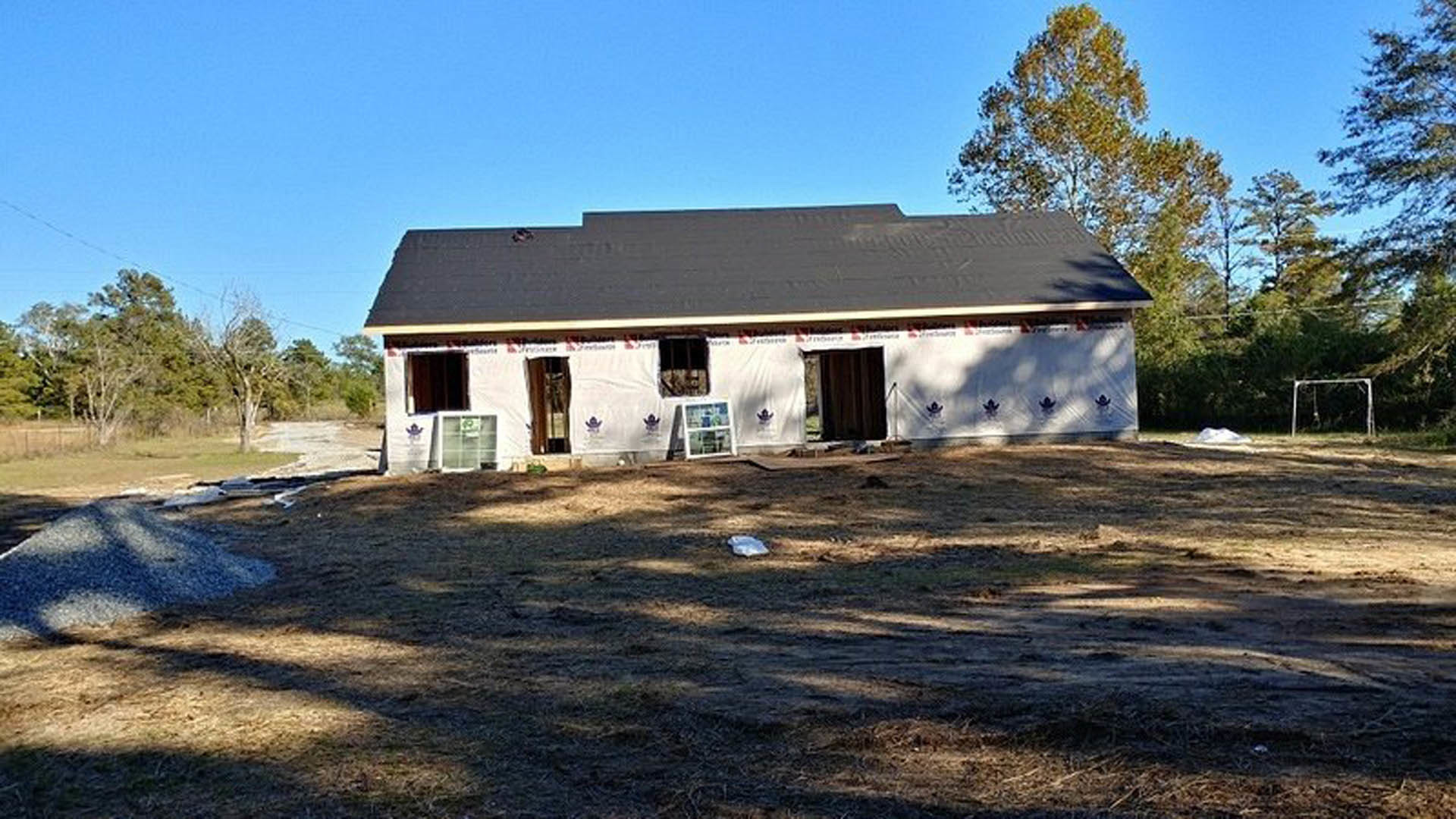 Framed custom home under construction with exposed wood, unfinished roof, and surrounding trees in the background