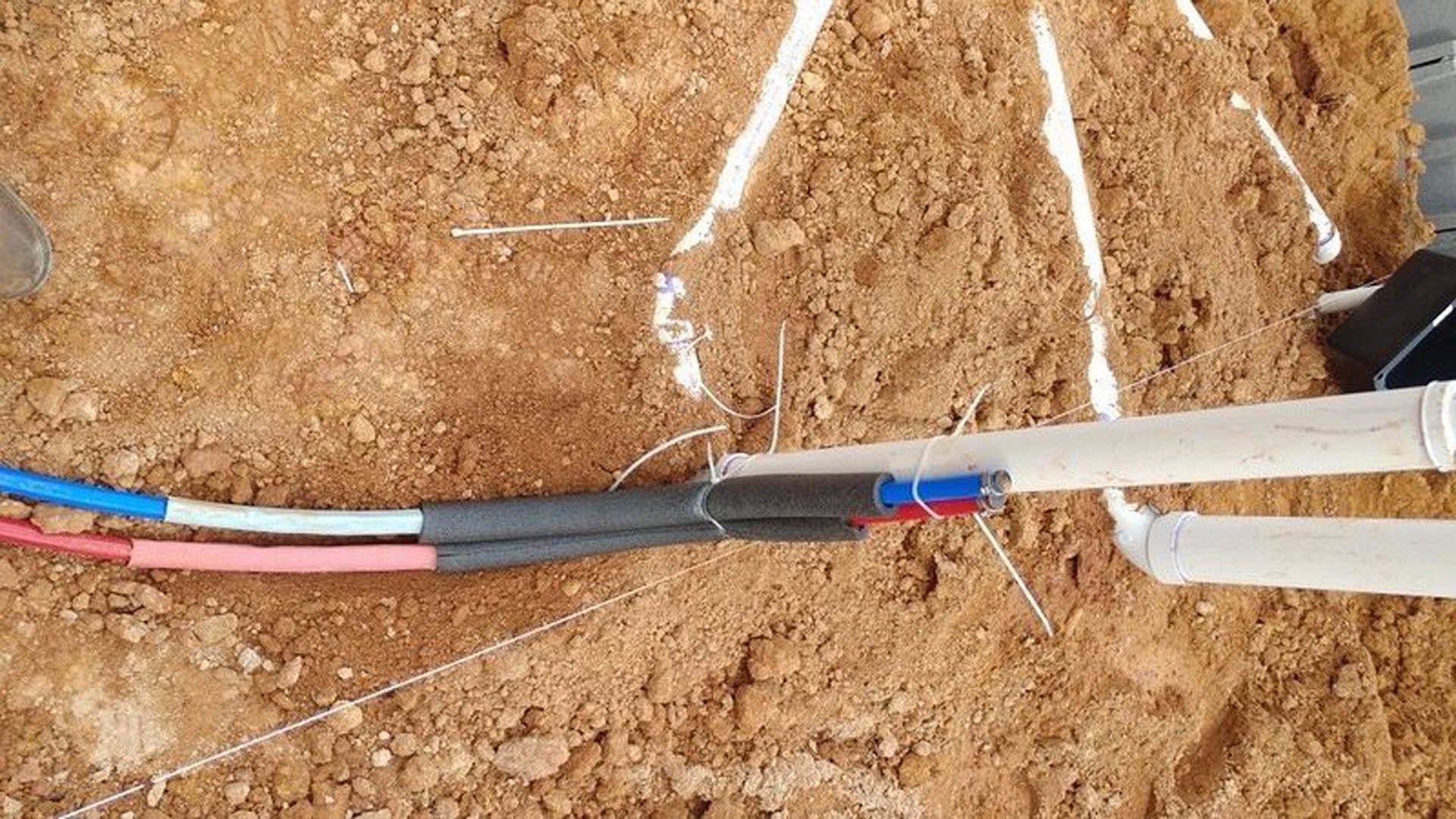 Close-up of a white electrical cable connected to a metal pipe outdoors on the ground