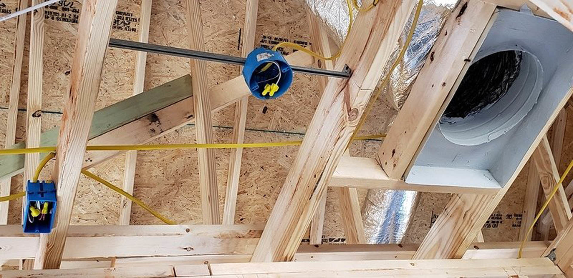 Wood beams under construction with a tape measure resting on top, vent installed in roof, ladder positioned nearby on exterior.