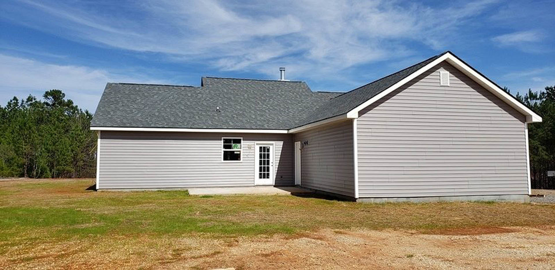 Two-story house with gray siding, white trim, front door, brick chimney, and manicured green lawn under partly cloudy sky