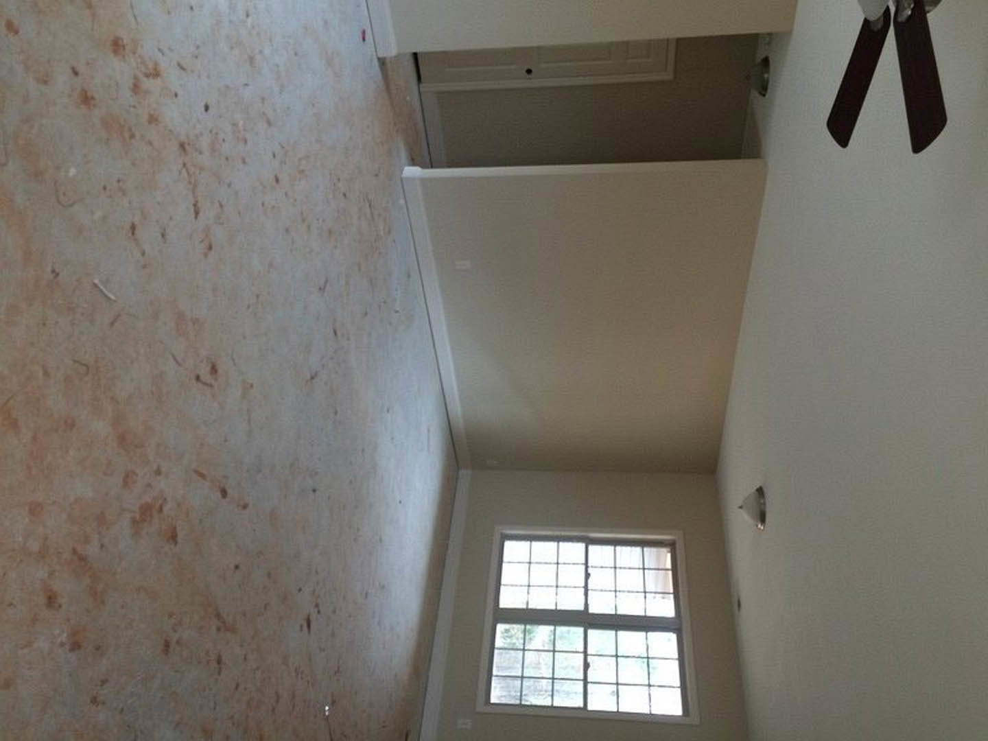 Bright room with white plaster walls, black door, multi-pane window, light wood flooring, and ceiling fan with black blades