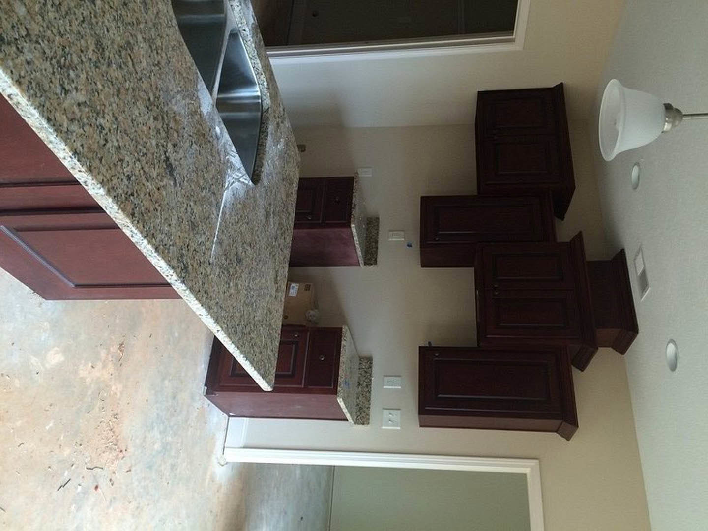 Granite countertops, dark wood cabinets, stainless steel sink, light fixture mounted on wall, close-up of polished stone surface, dark wood paneling with integrated lighting