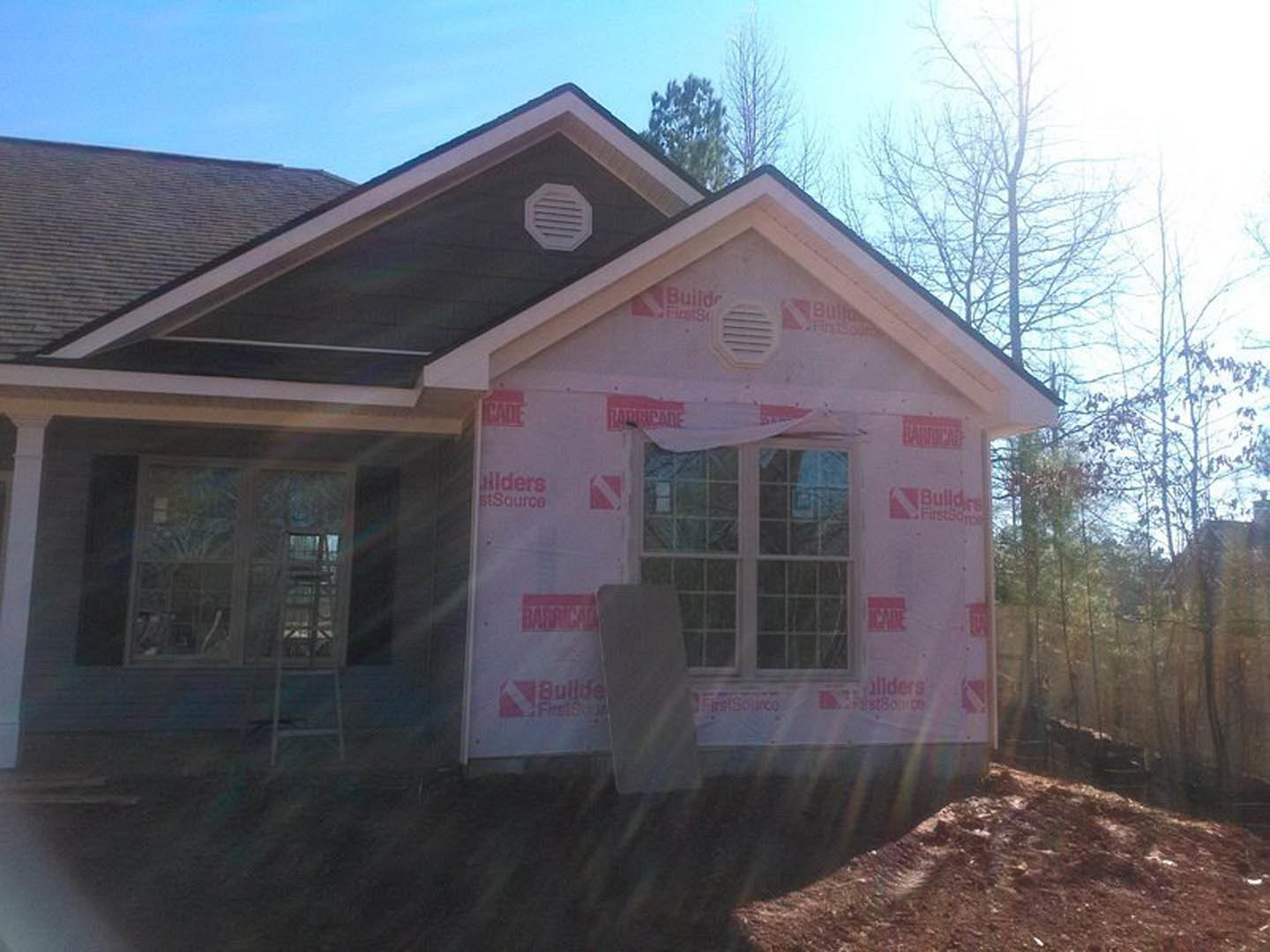 White siding house under construction with red tape along exterior wall, window covered by pink cloth, white vent installed near door, tree visible in background.