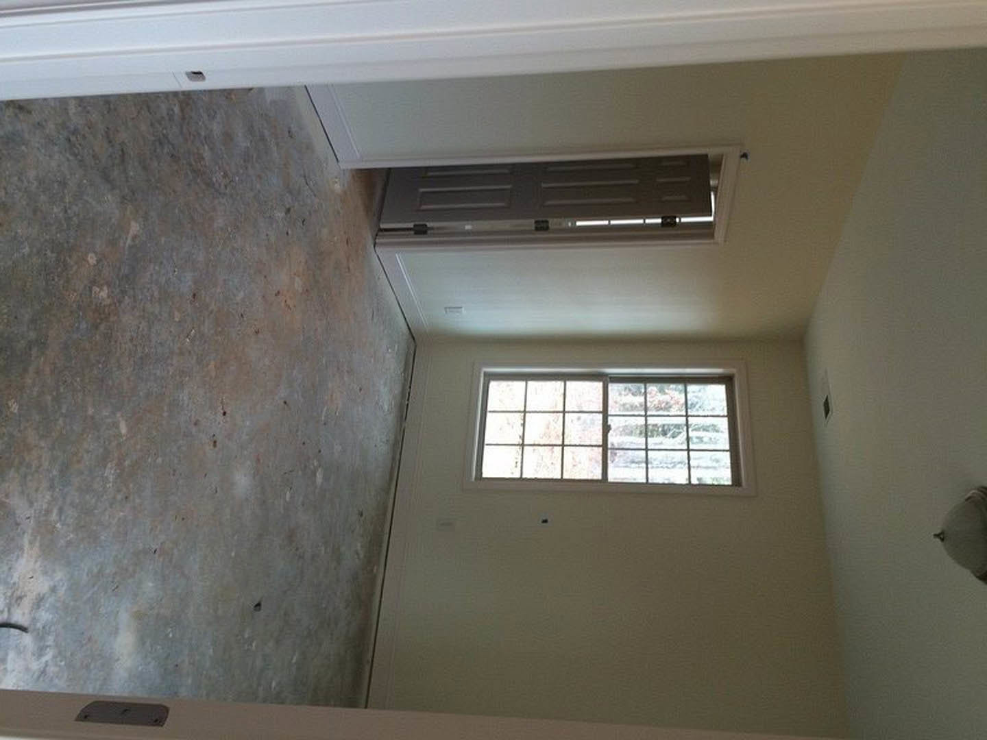 Modern interior room featuring a white plaster wall, large window with outdoor view, concrete floor, and sleek door