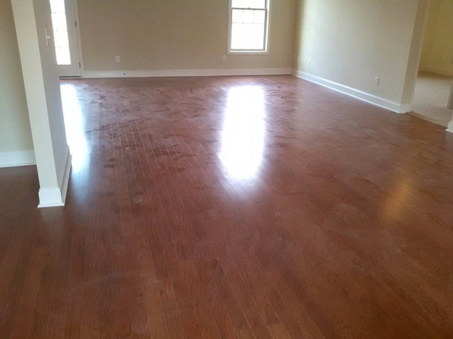 Sunlit room with white walls, large window with white frame, and polished wood flooring; person standing near the wall.
