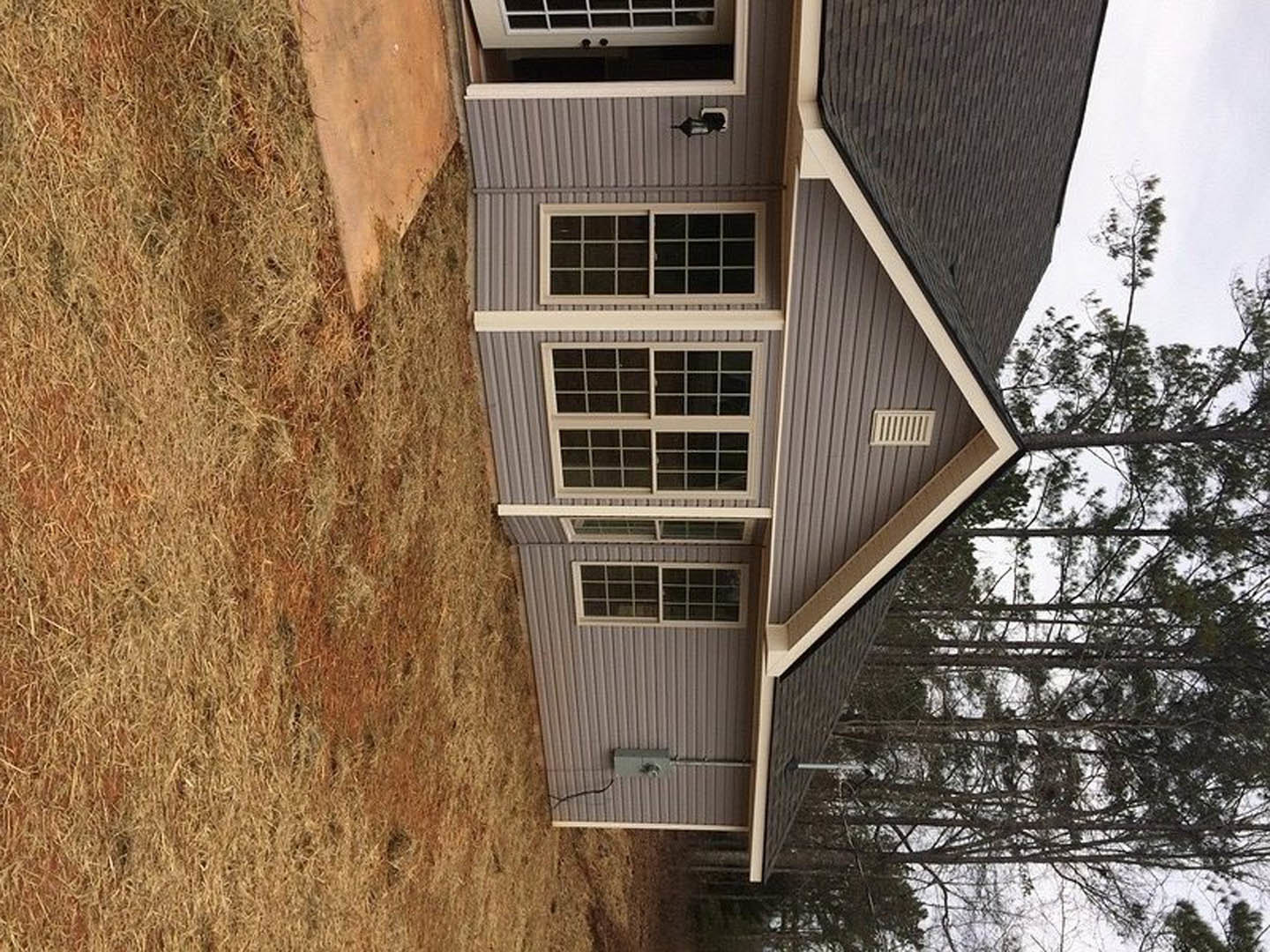 Red brick exterior with white trim, multi-pane window, concrete patio, and grassy yard bordered by mature trees