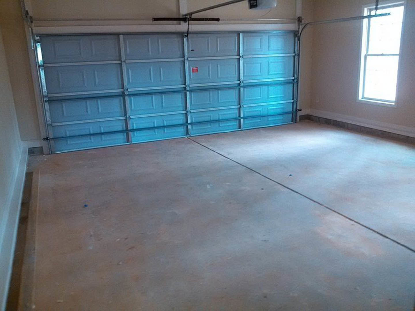 Garage interior with blue door, concrete floor, window letting in daylight, black pipe along wall, red sign on blue wall, partial view of person’s head in foreground.