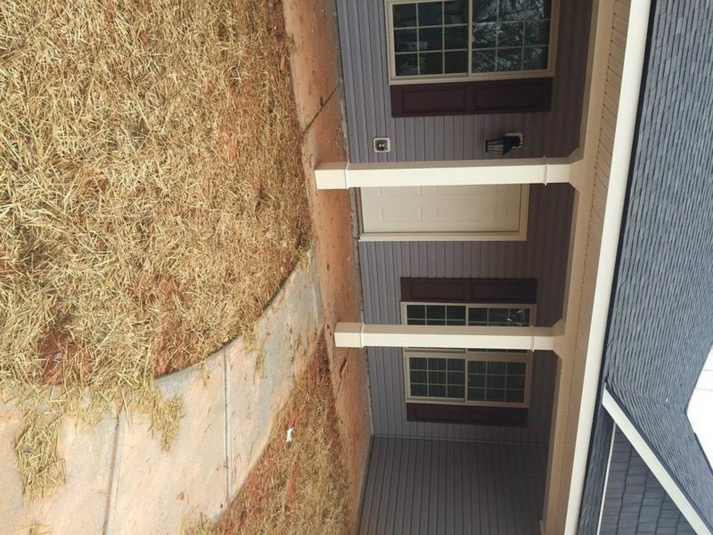 White house exterior with glass windows, white pillars, front door, and grassy yard bordered by hay.