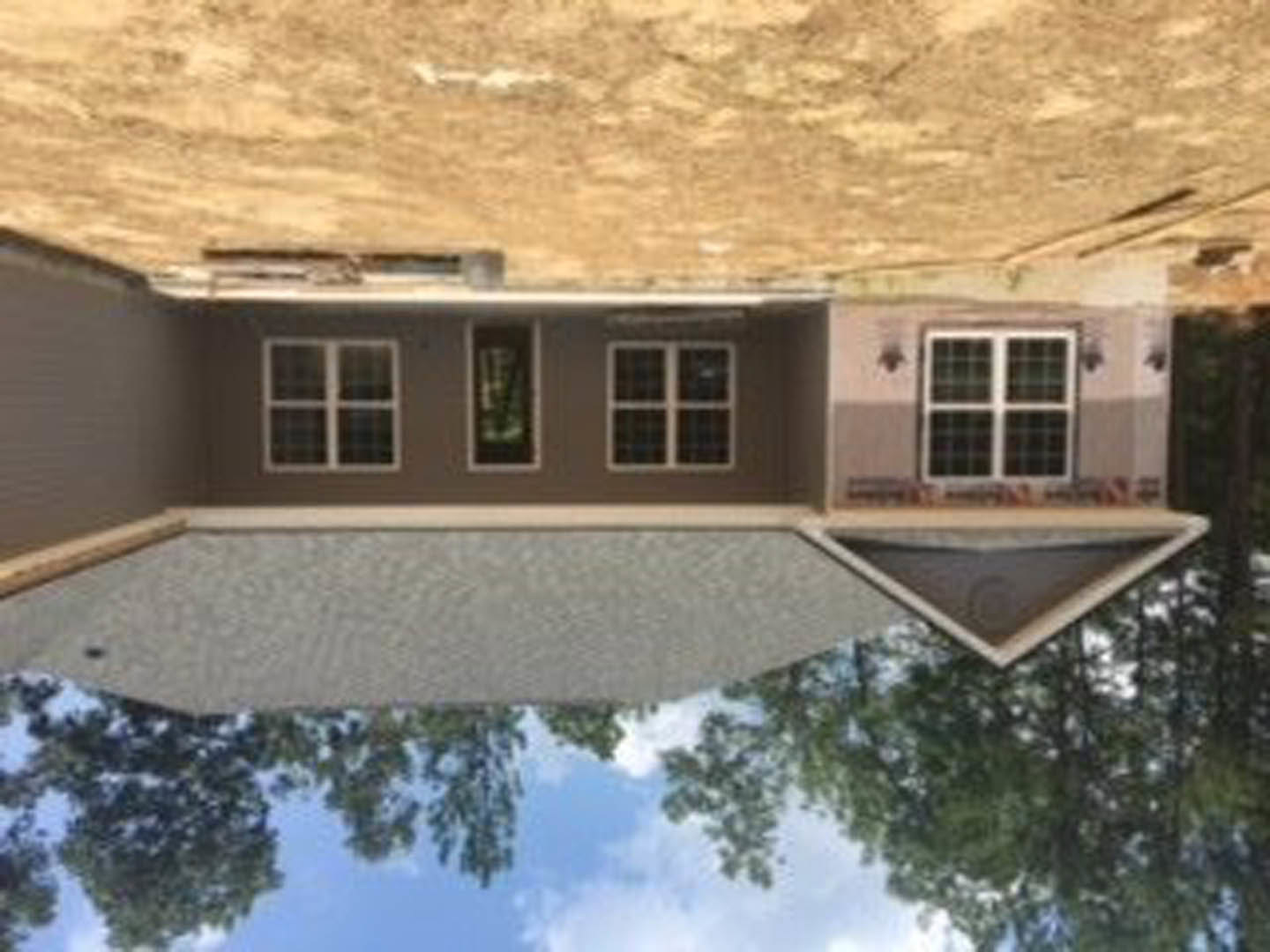 Two-story house with white siding, dark roof shingles, large windows, and mature trees in the background