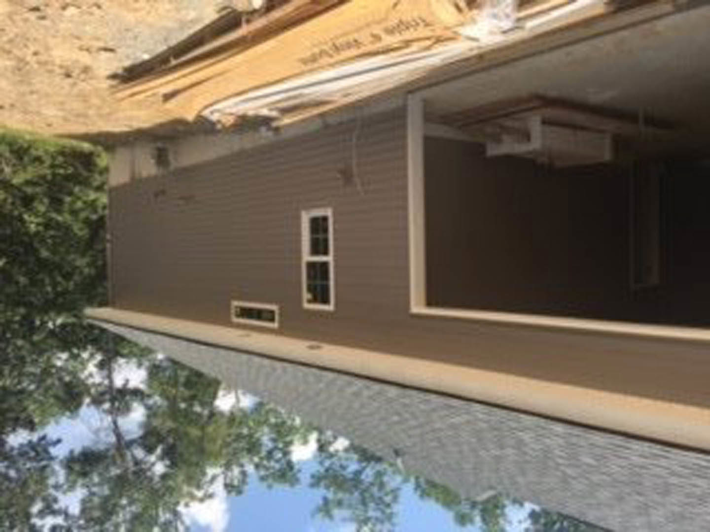 Modern home exterior with open front door, large windows, white siding, and mature trees in the background