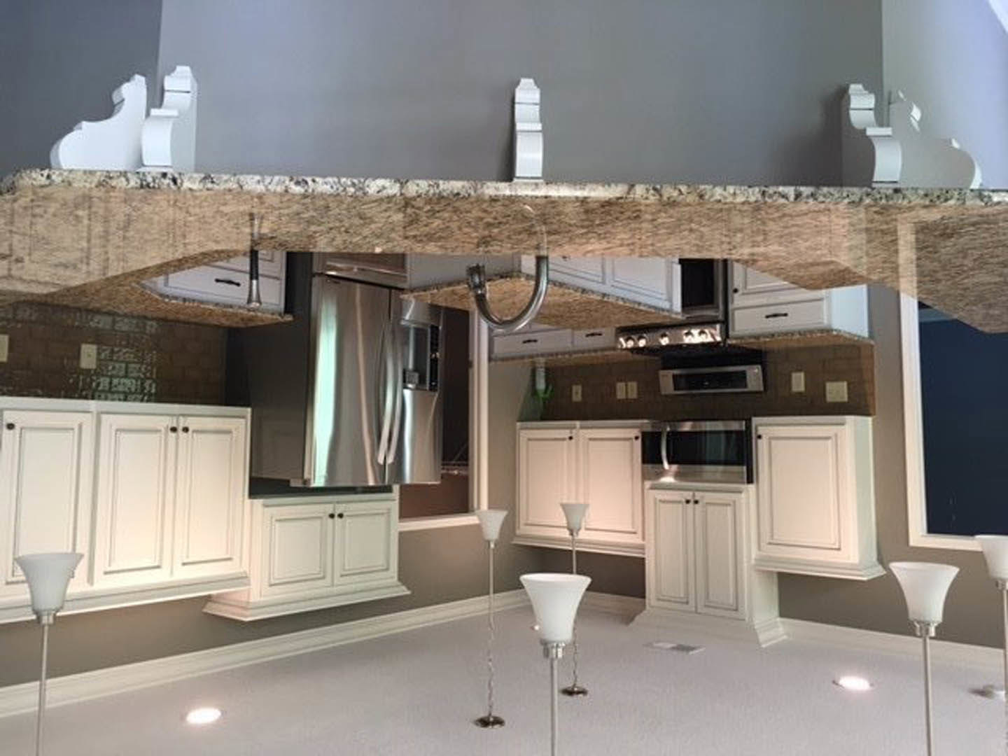 Marble countertops and white cabinetry in a modern kitchen with stainless steel refrigerator, white ceiling, and silver pendant lamp