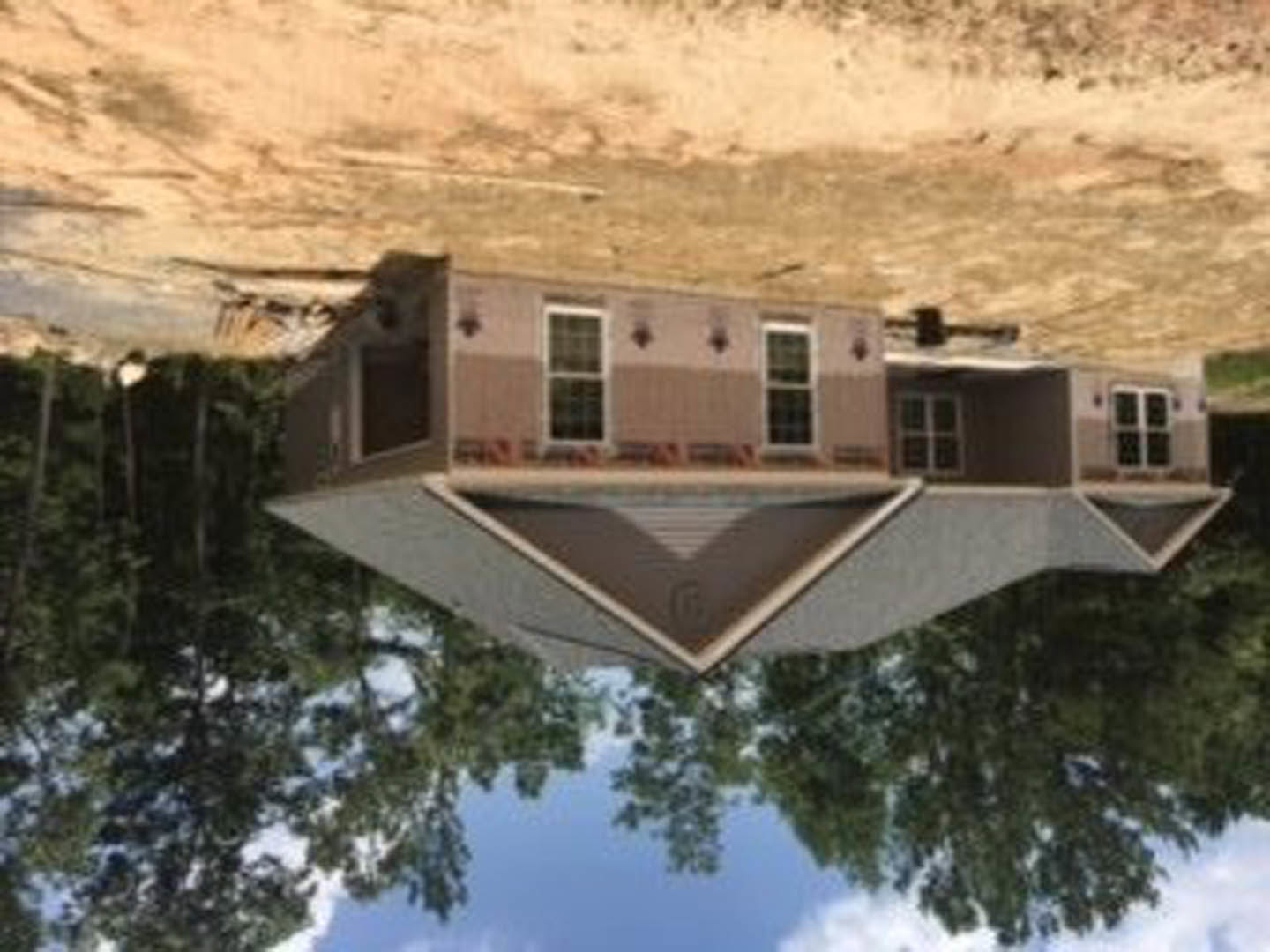 Two-story home with white-framed windows, light siding, and gabled roof, surrounded by mature trees and mountain backdrop under partly cloudy sky