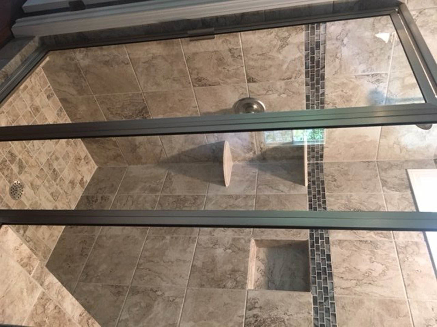 Walk-in shower with clear glass doors, built-in bench, large window, and light gray tile floor with a square drain