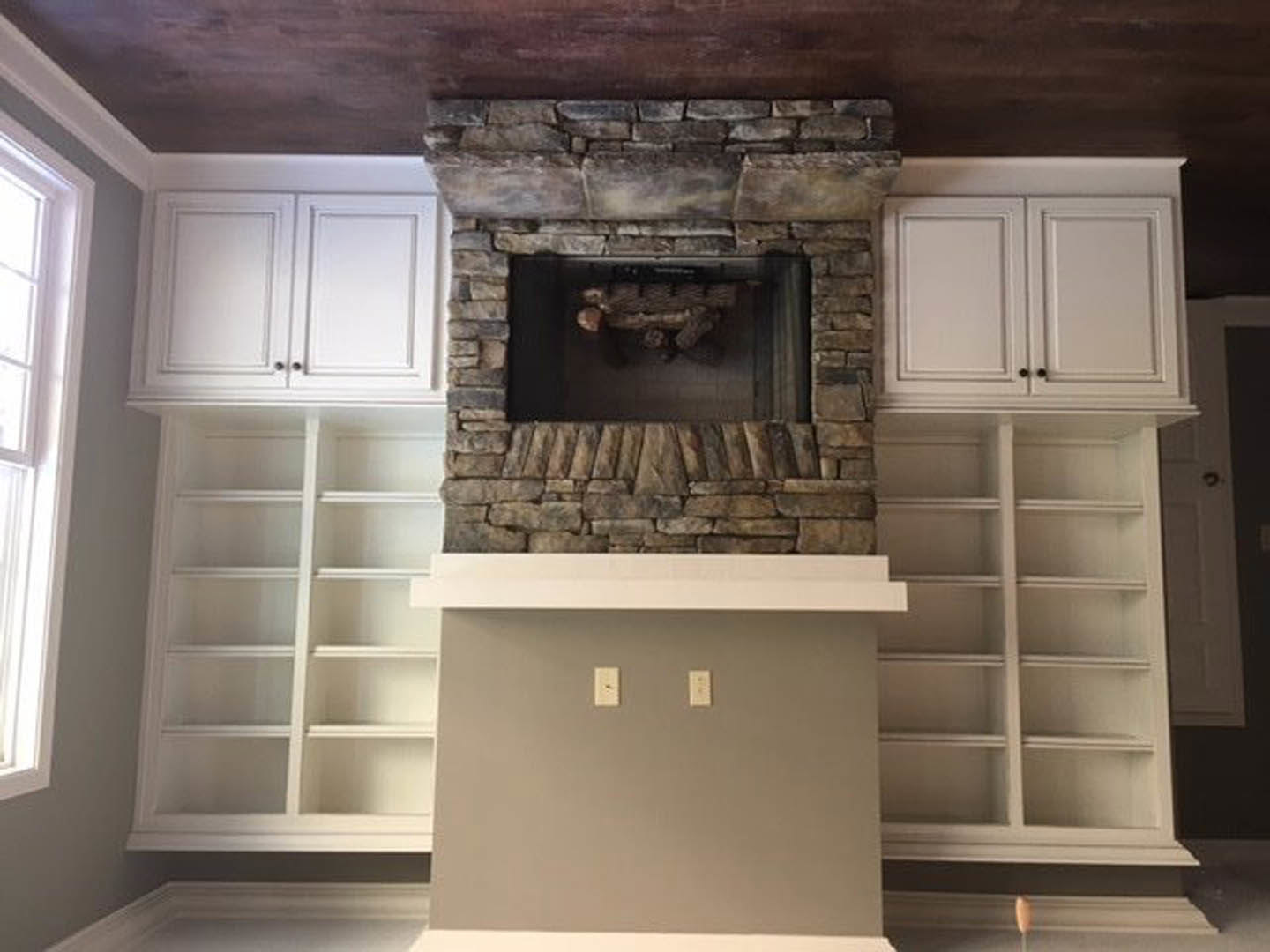 Fireplace with glass window set in a room featuring white cabinetry, built-in shelves, and decorative molding; light switches visible on adjacent wall, person in suit standing