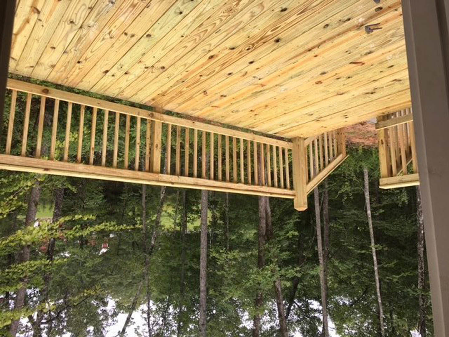 Wooden deck with railing and ladder, surrounded by trees and a wooden fence