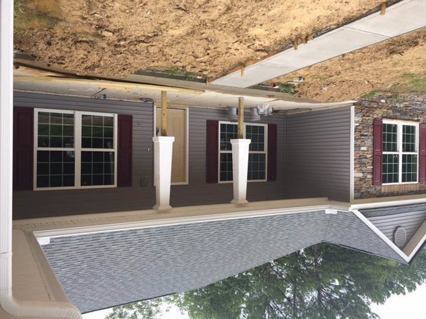 Red brick exterior with white-framed window, white pillar featuring black and white base, and a white vase on the porch; gabled roof and mature tree in front yard