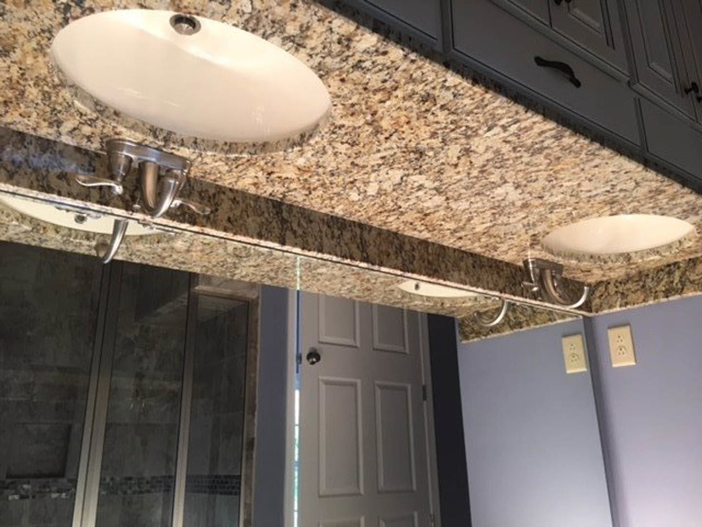 Bathroom countertop with two white sinks, chrome faucets, tiled backsplash, and wall-mounted fixtures