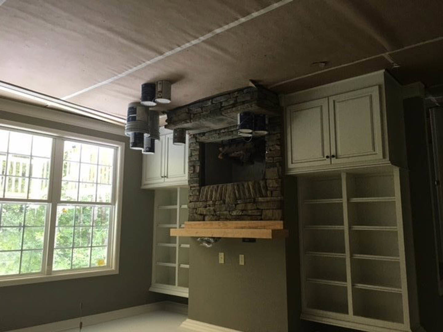 Living room with built-in white shelves flanking a stone fireplace, multi-pane window, wood flooring, and recessed ceiling lighting