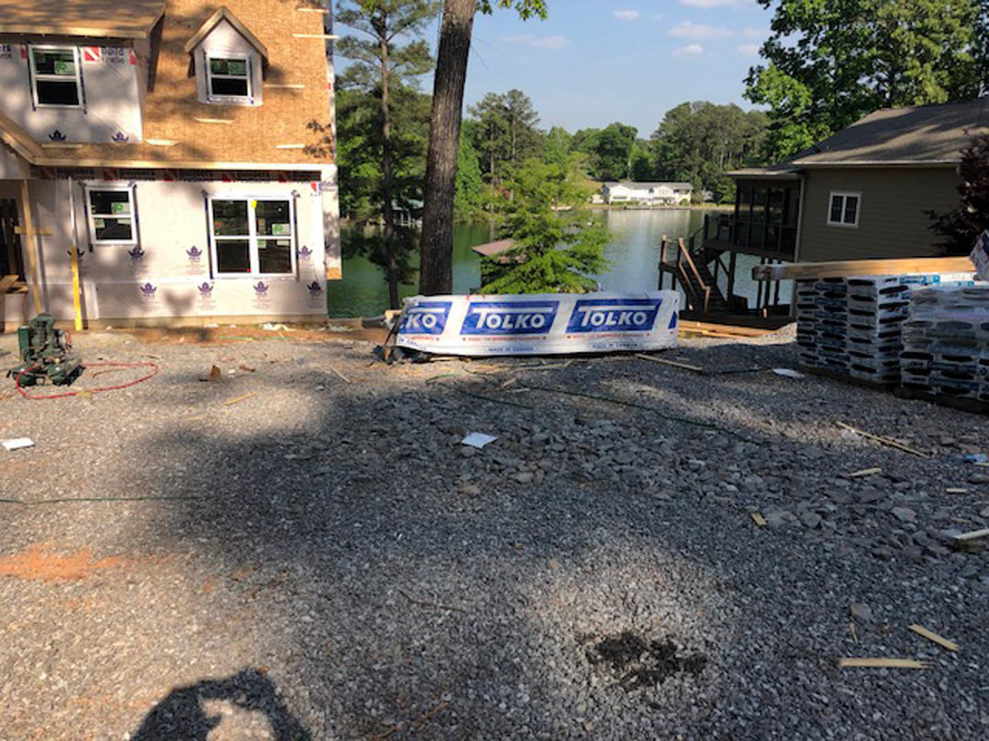 Modern lakeside house with large white-framed windows, gravel landscaping, and black and orange staircase visible near the entrance.