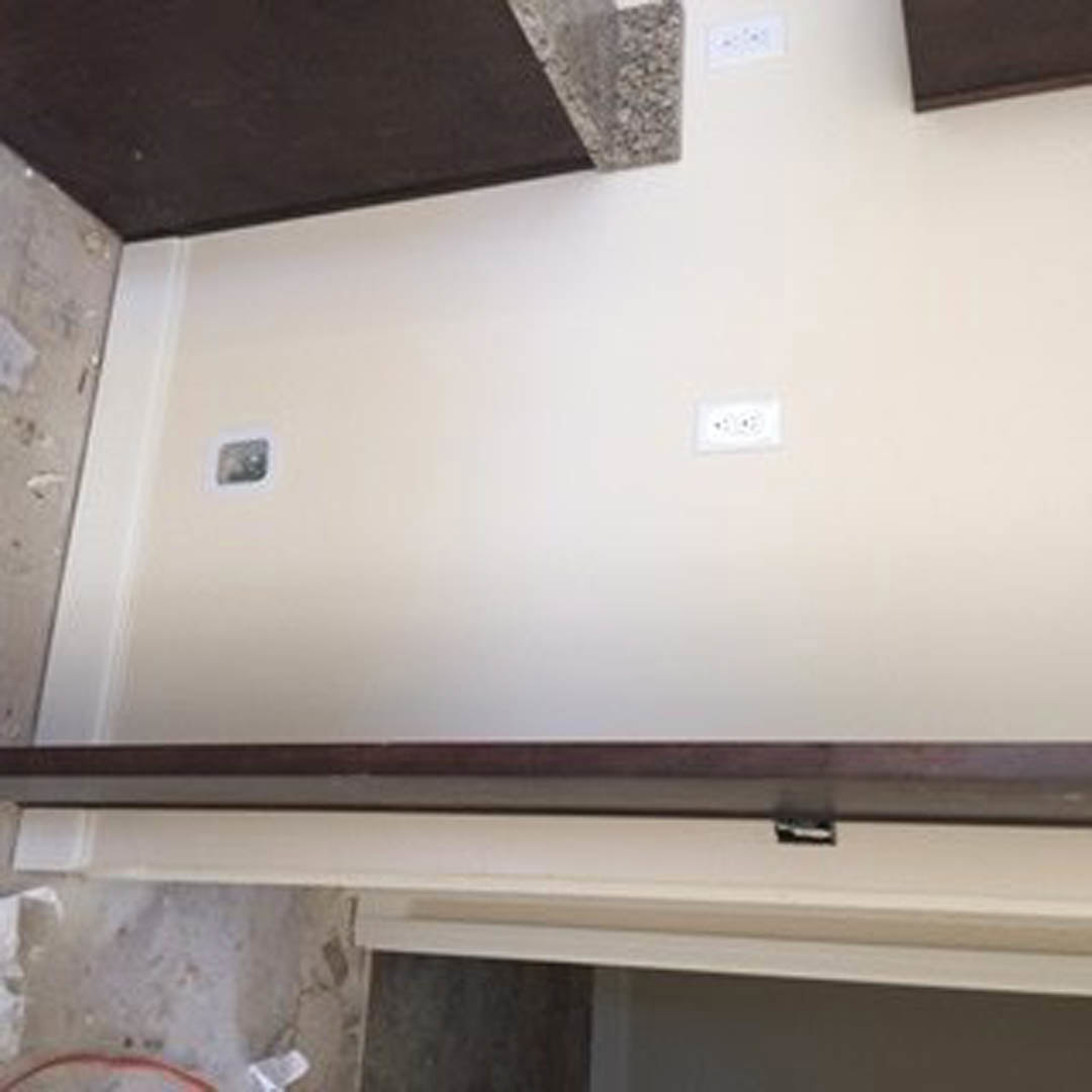 White wall with floating black shelf and multiple electrical outlets, including a white outlet with black buttons.