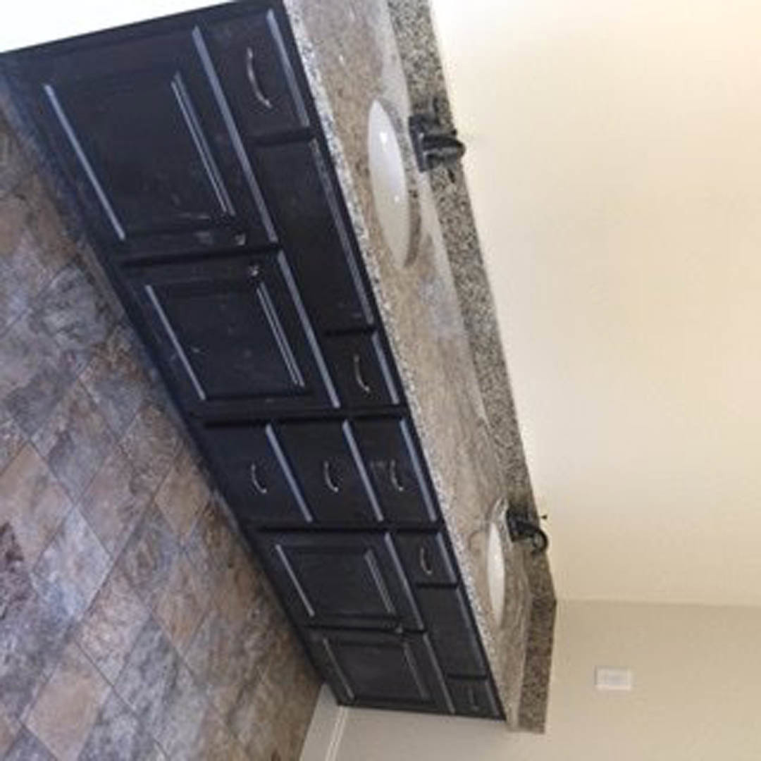 Bathroom featuring a marble countertop with undermount sink, white cabinetry, and tiled wall.