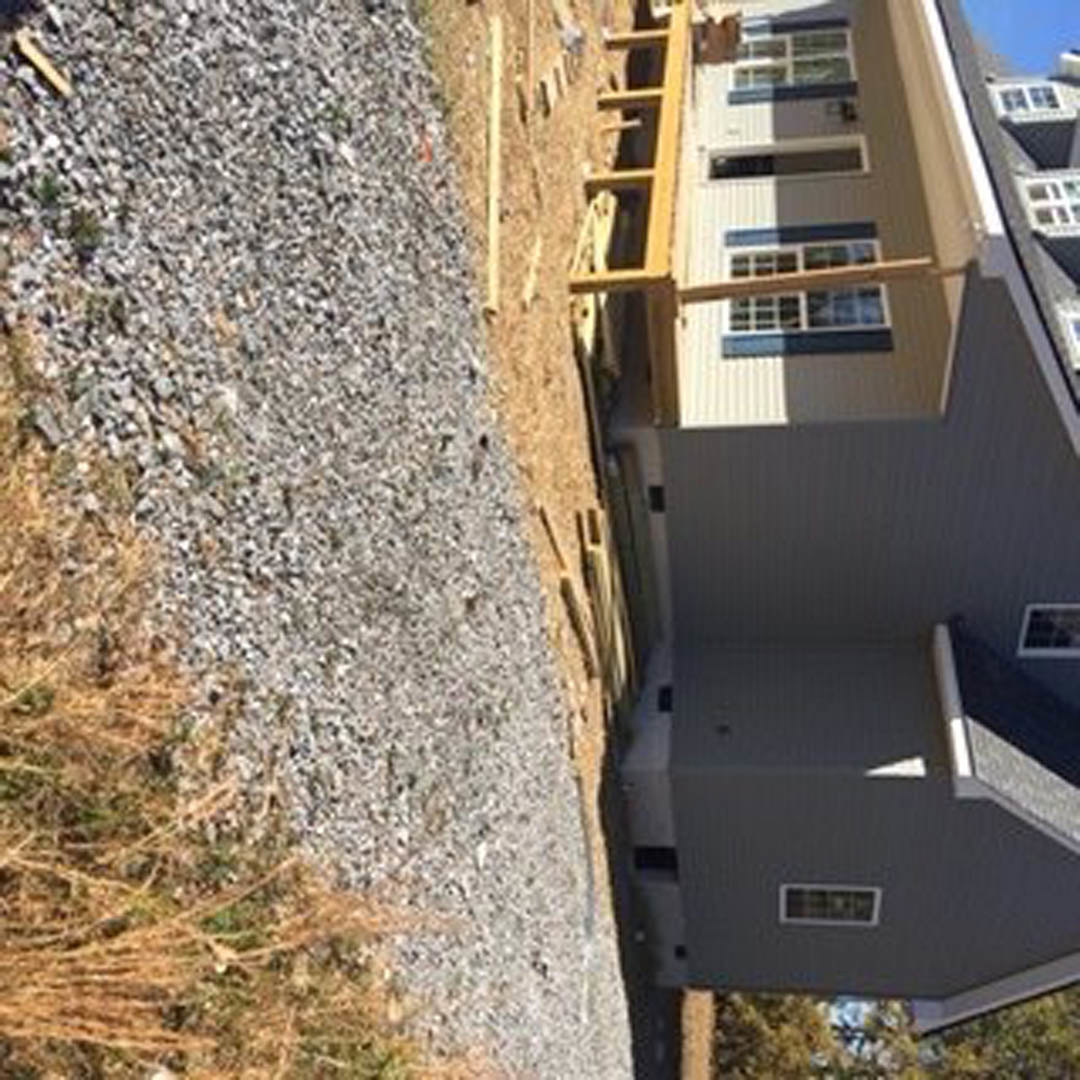 Partially built house with exposed wooden beams, multiple windows, fenced yard, gravel and grass surrounding the construction site