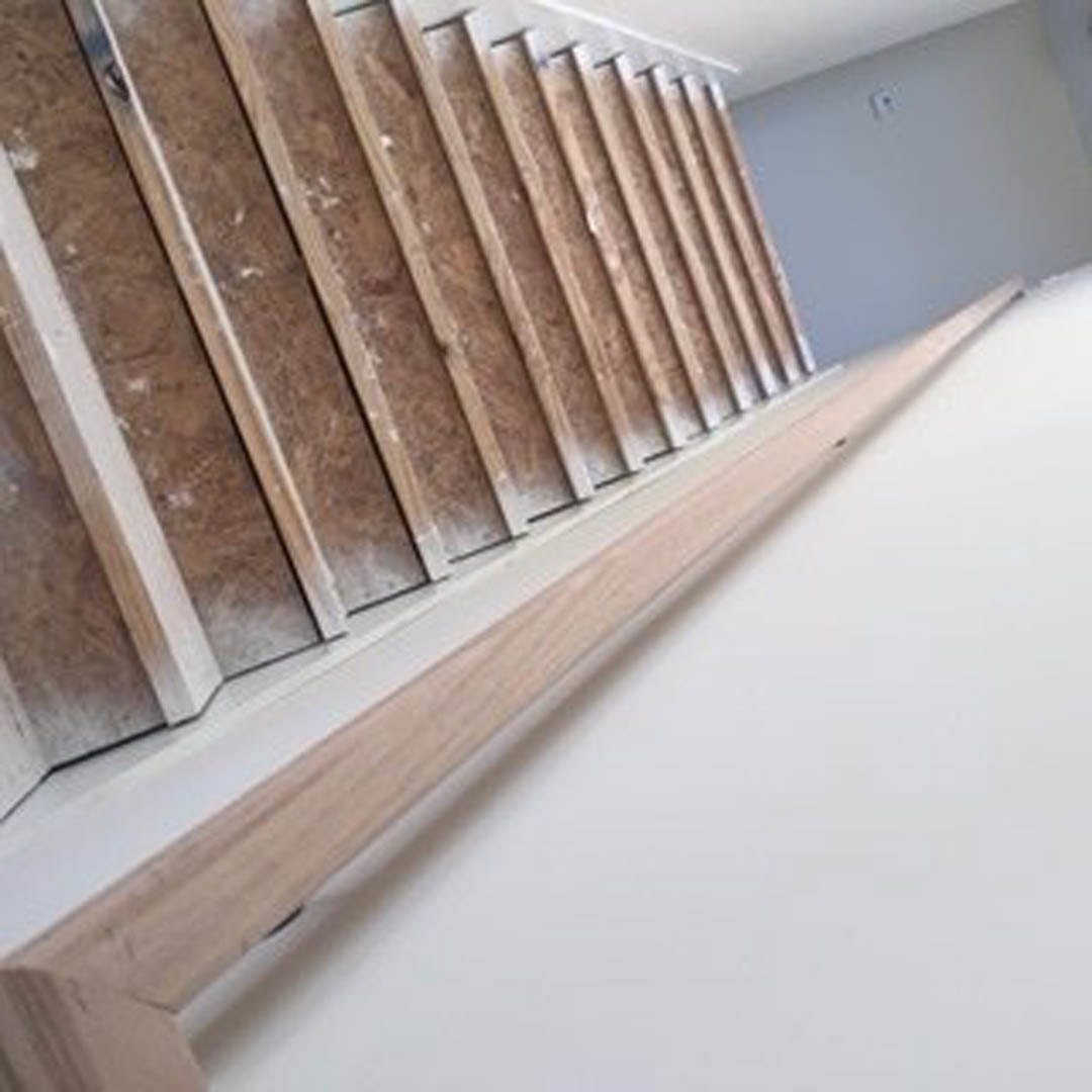 Wood plank staircase with plywood wall, hardwood treads, and white surface featuring a small black dot