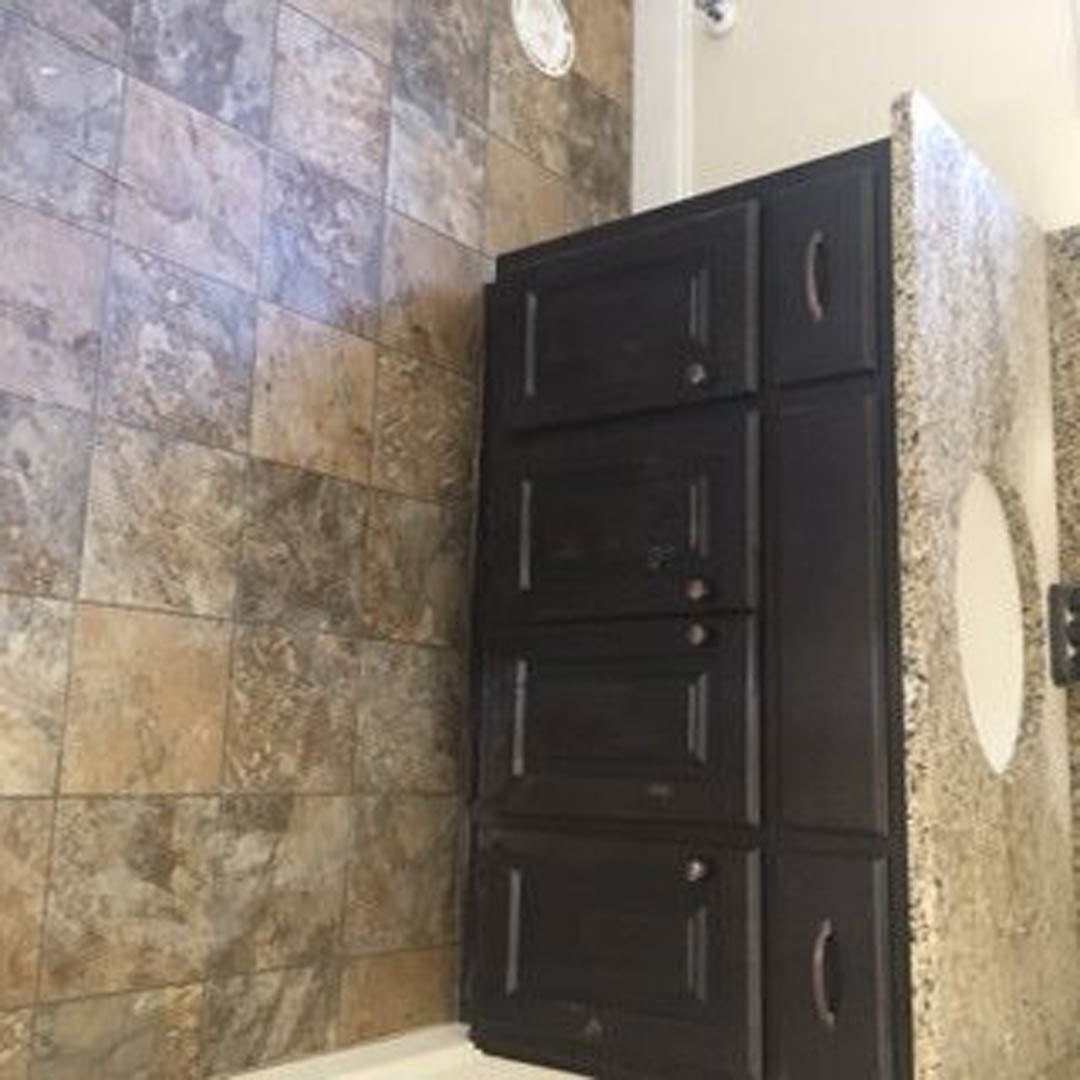 Marble bathroom countertop with white cabinetry, black trim accents, tile flooring, and soft natural light illuminating the space.