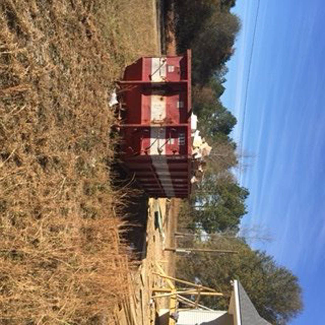 Red and white shipping container with vertical stripes set on grassy field, surrounded by trees under open sky.