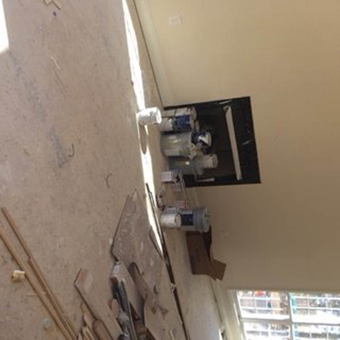 White-walled room with stacked white paint cans on the floor, white electrical outlet on the wall, and blurred figure in the background.