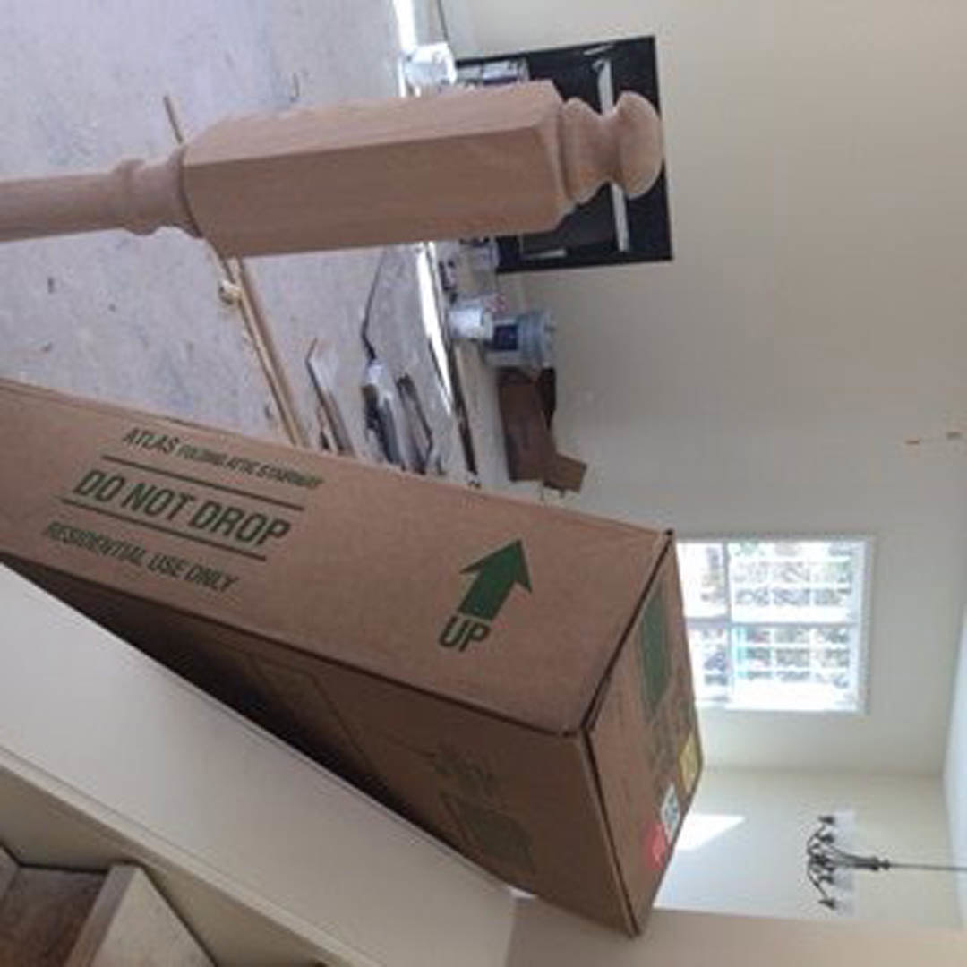 Cardboard shipping box with green text mounted on a wooden post indoors, wall and window visible in background