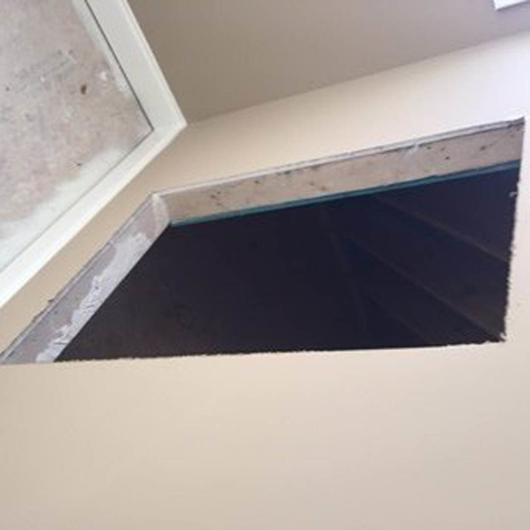 White plaster wall with a rectangular hole revealing a black screen, surrounded by smooth white surfaces in a modern interior.